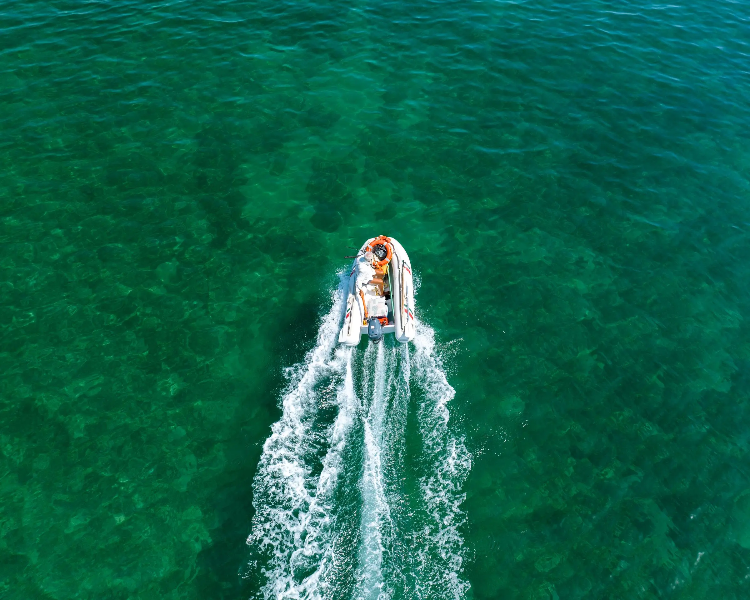Gommone bianco visto dall'alto che corre su un mare verde smeraldo, lasciando una lunga scia bianca