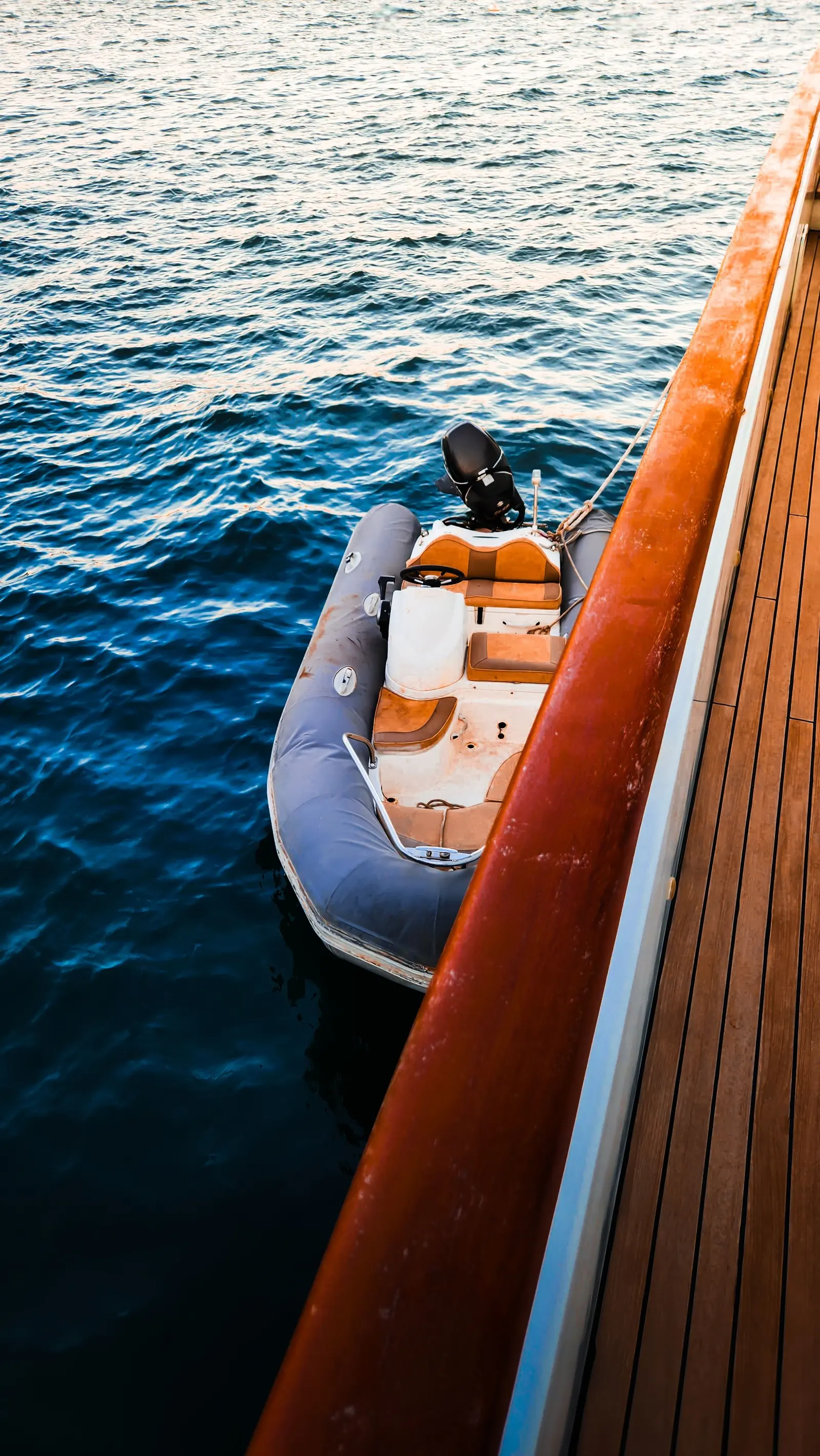 Piccolo gommone accostato al fianco in legno di uno yacht, visto dall'alto sull'acqua blu