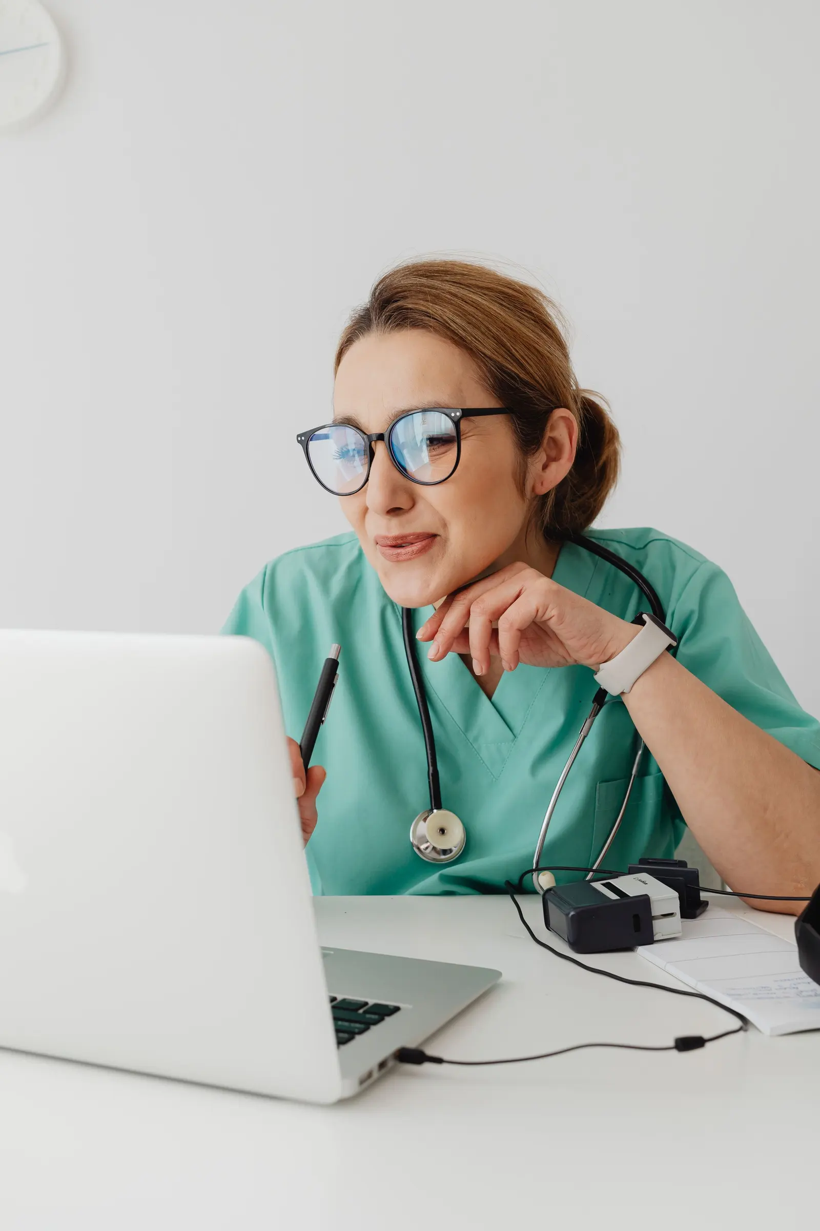 Una professionista sanitaria in casacca verde acqua sorride davanti al portatile, alla scrivania