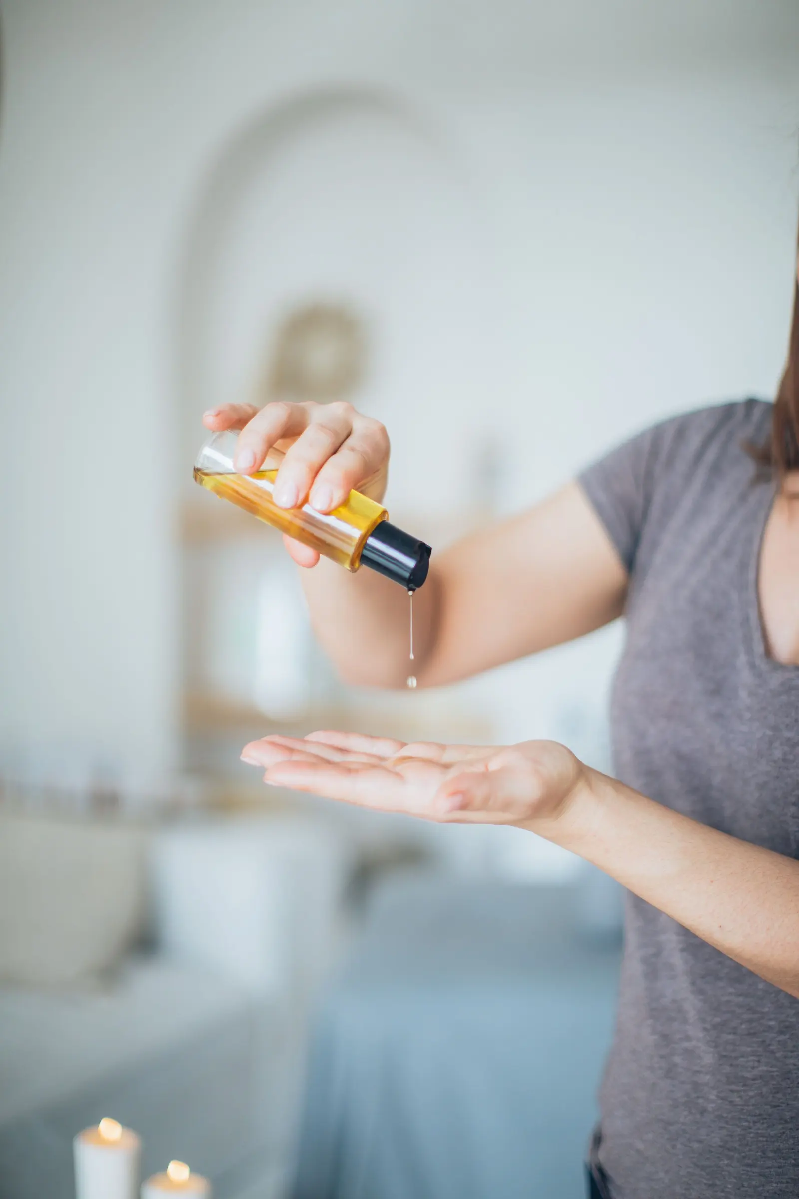Una mano versa qualche goccia d'olio sul palmo dell'altra, in una stanza chiara con candele