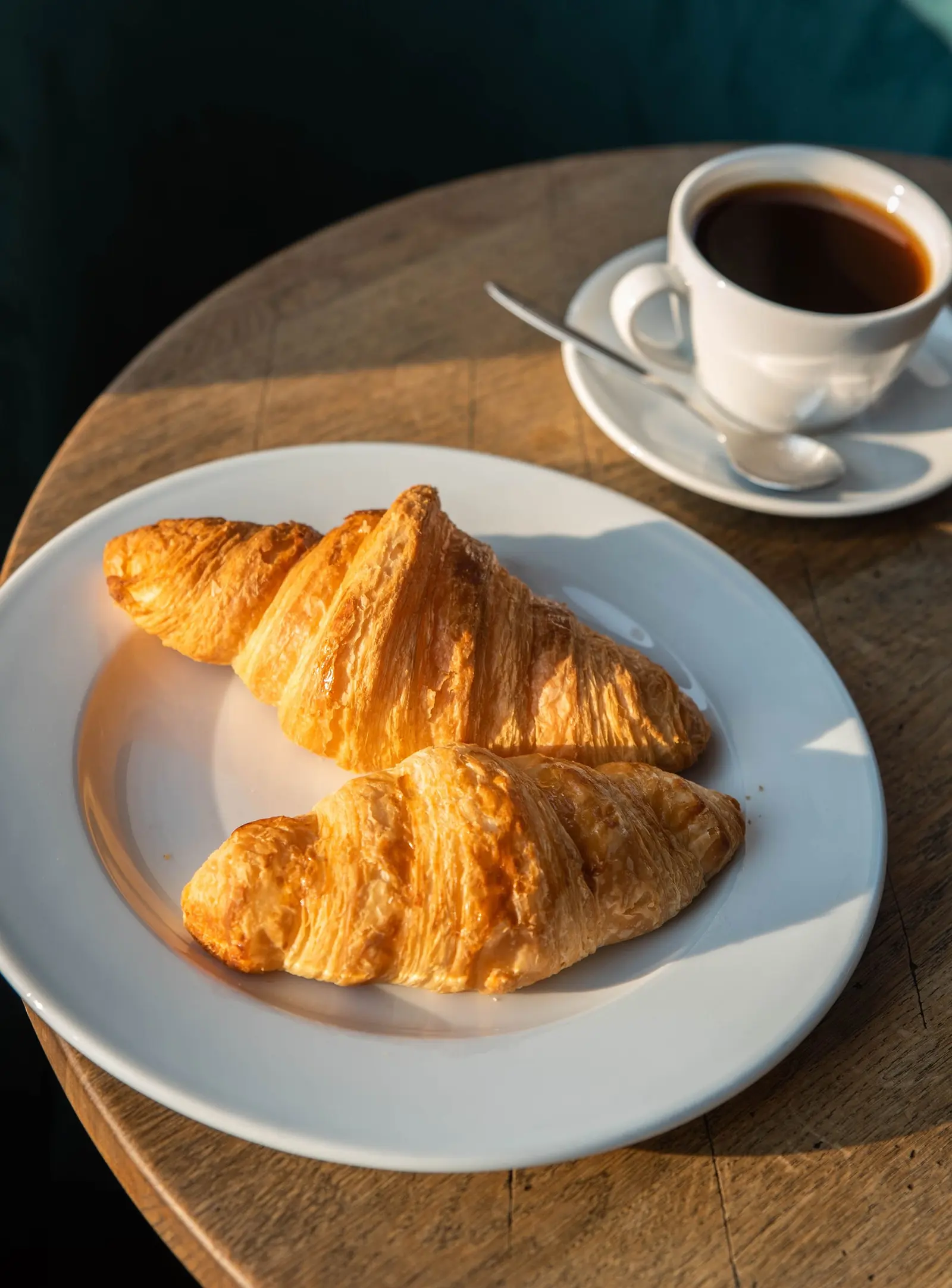 Due cornetti su un piatto bianco e una tazzina di caffè su un tavolino tondo di legno