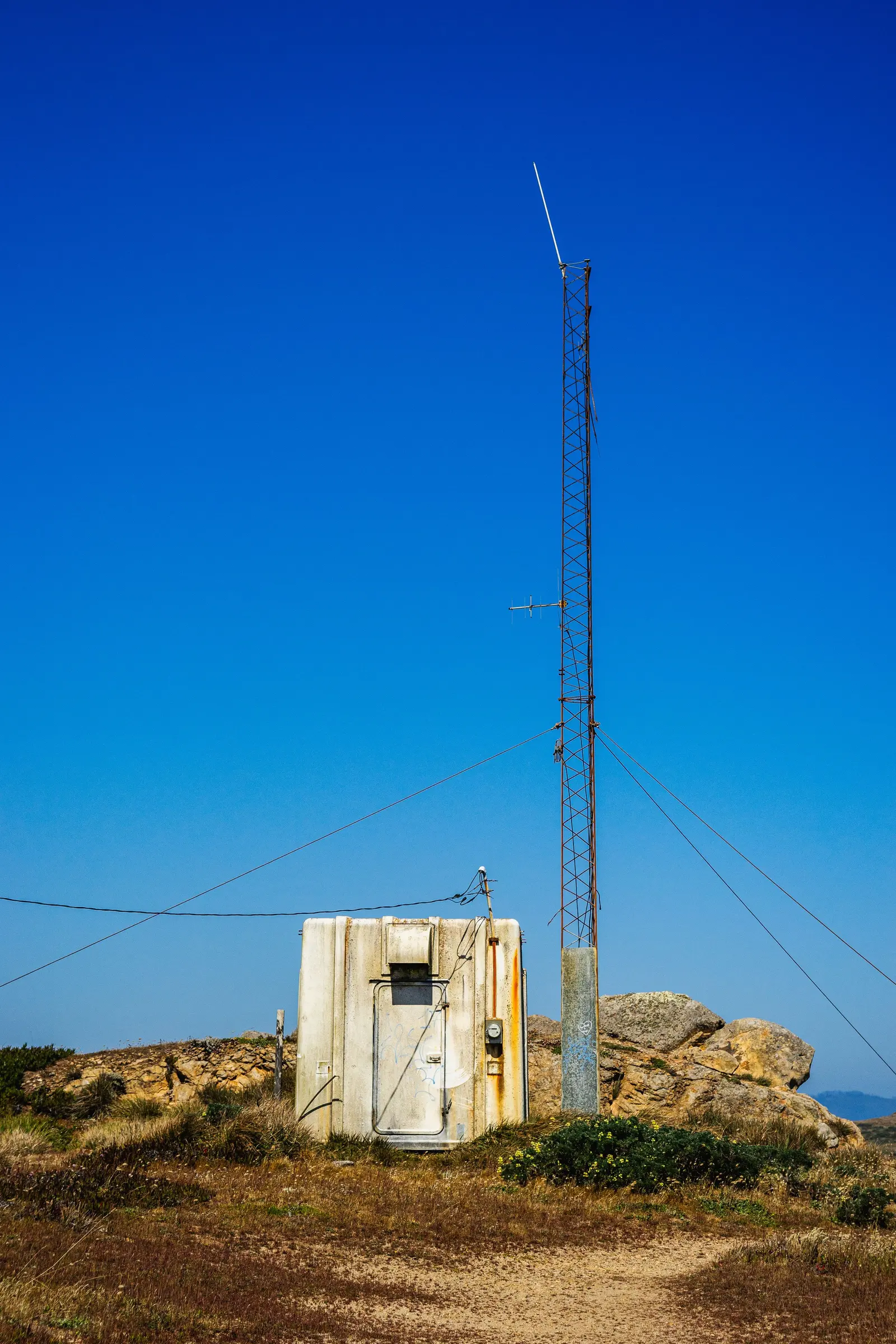 Un'antenna verticale strallata e uno shelter tecnico su un'altura rocciosa