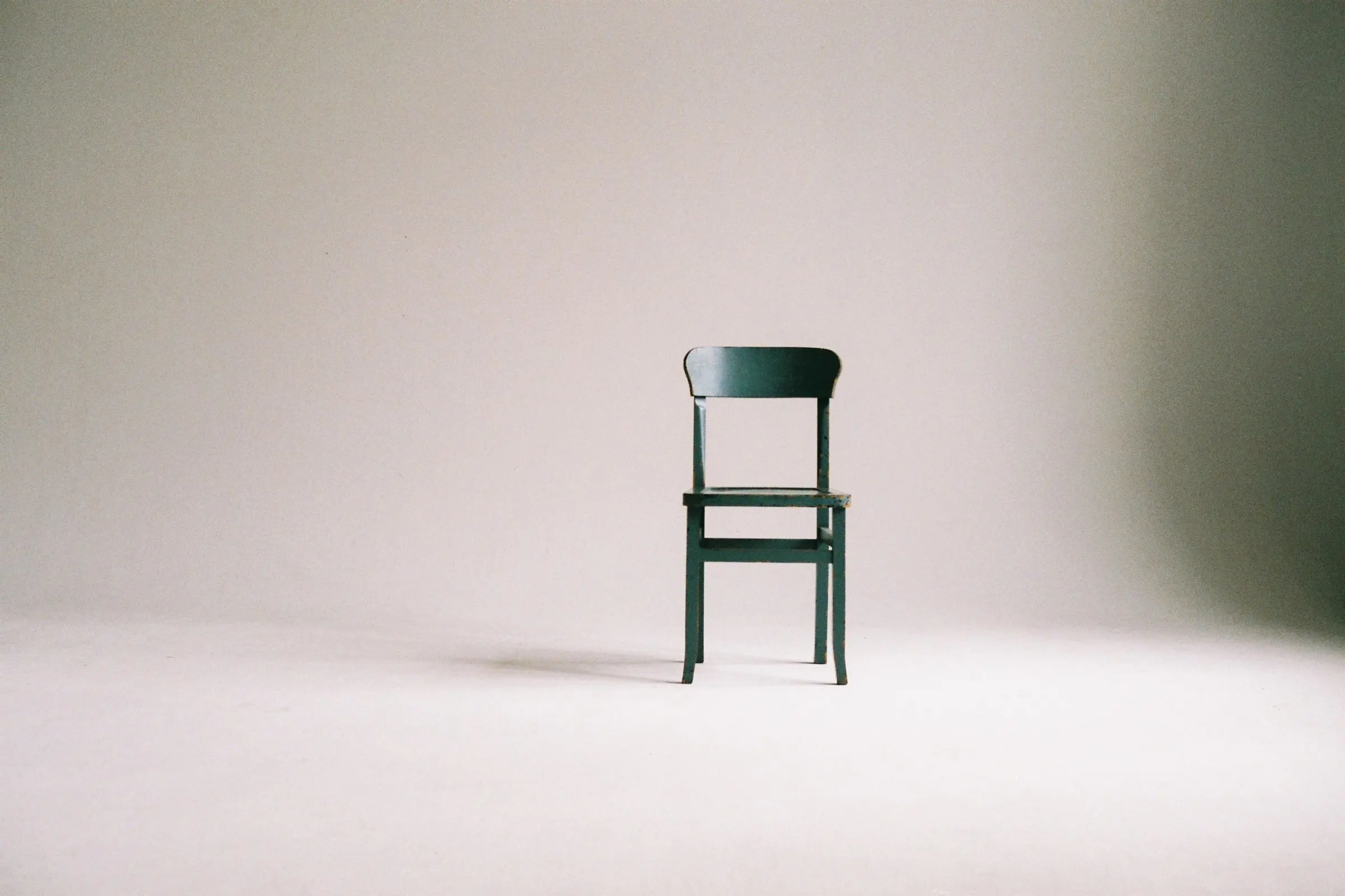 Una sedia in legno verde scuro, sola in uno studio fotografico bianco