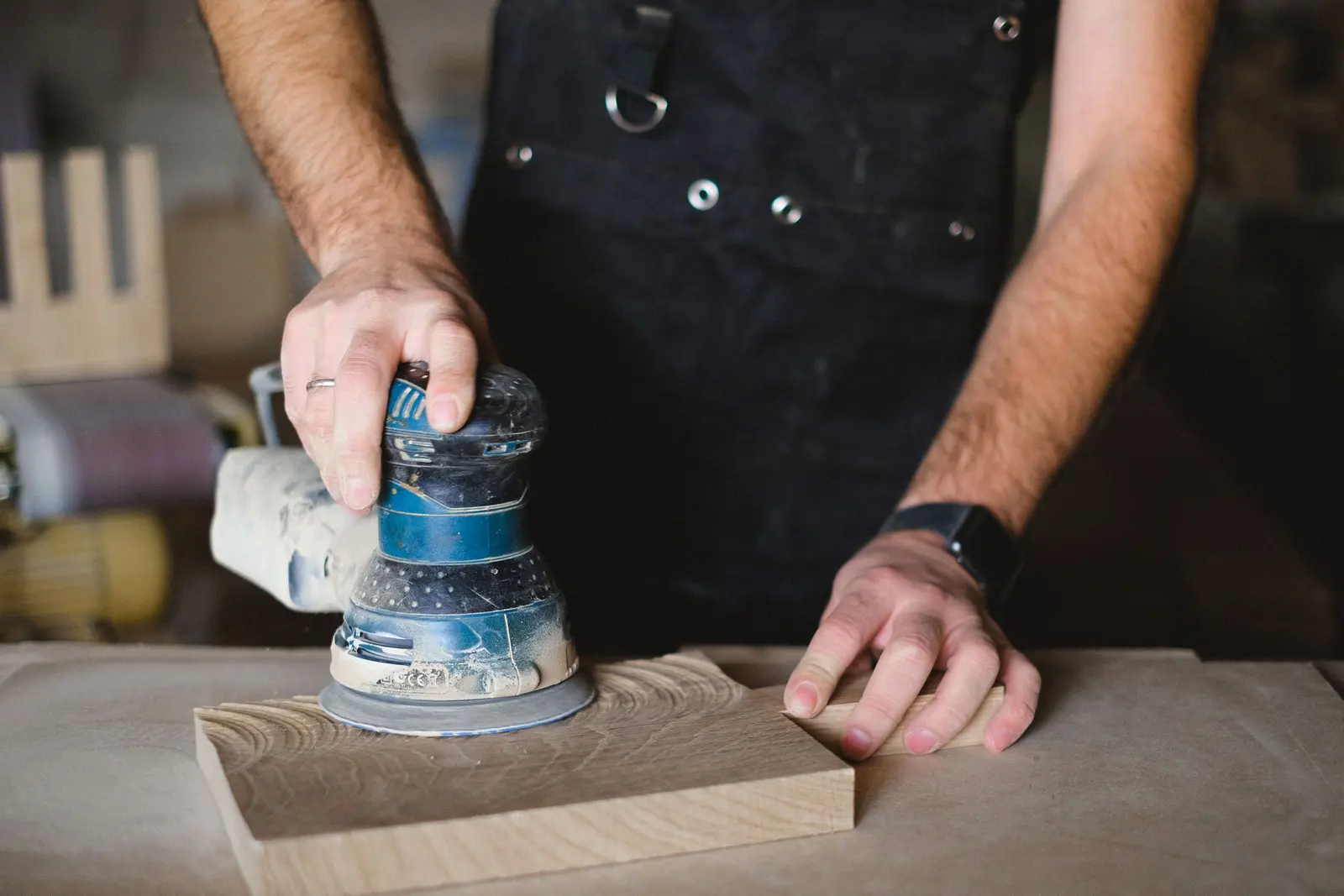 Mani con una levigatrice orbitale su un pezzo di legno chiaro