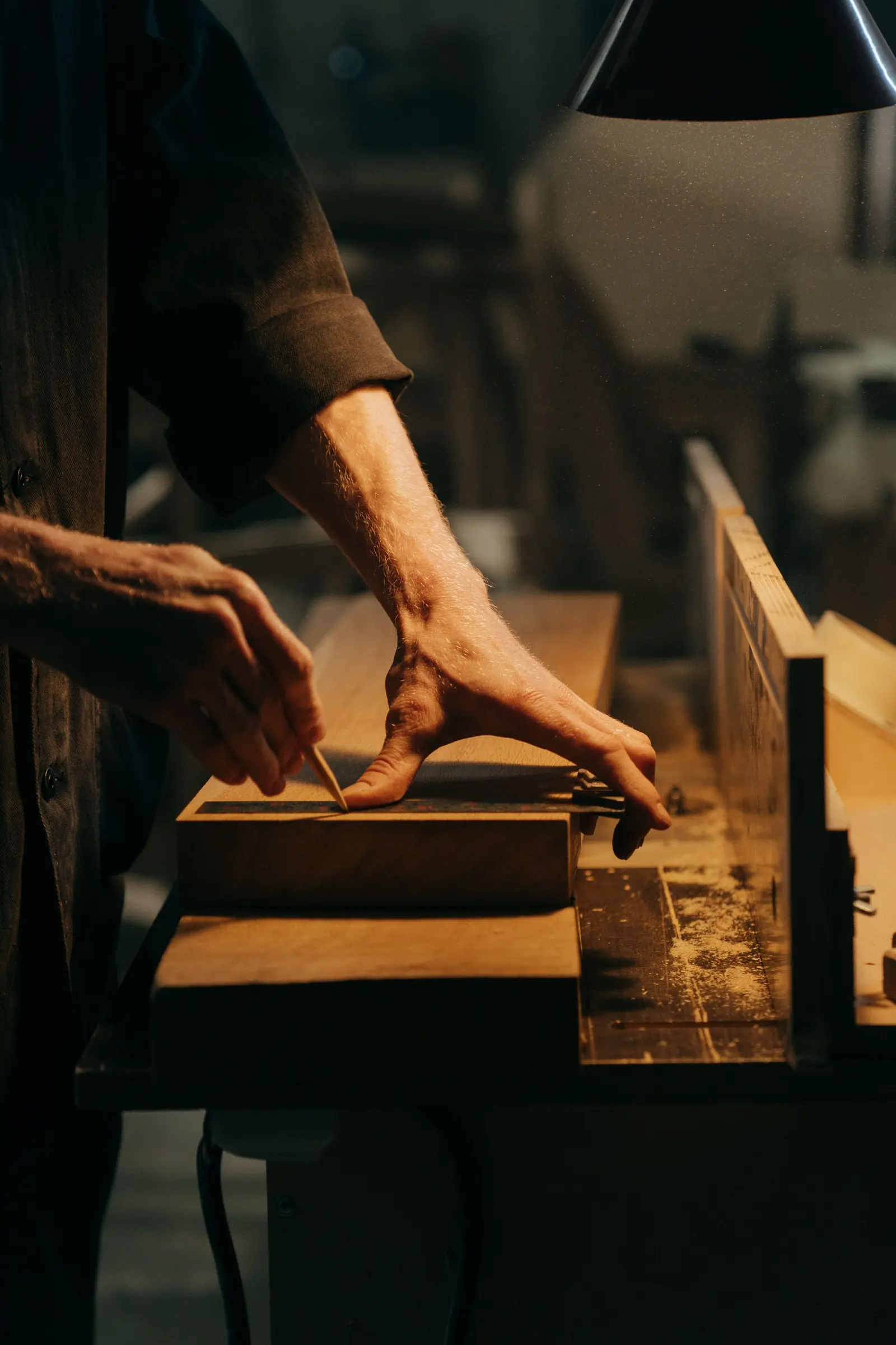 Mani che spingono un pezzo di legno su una sega da banco, in luce calda