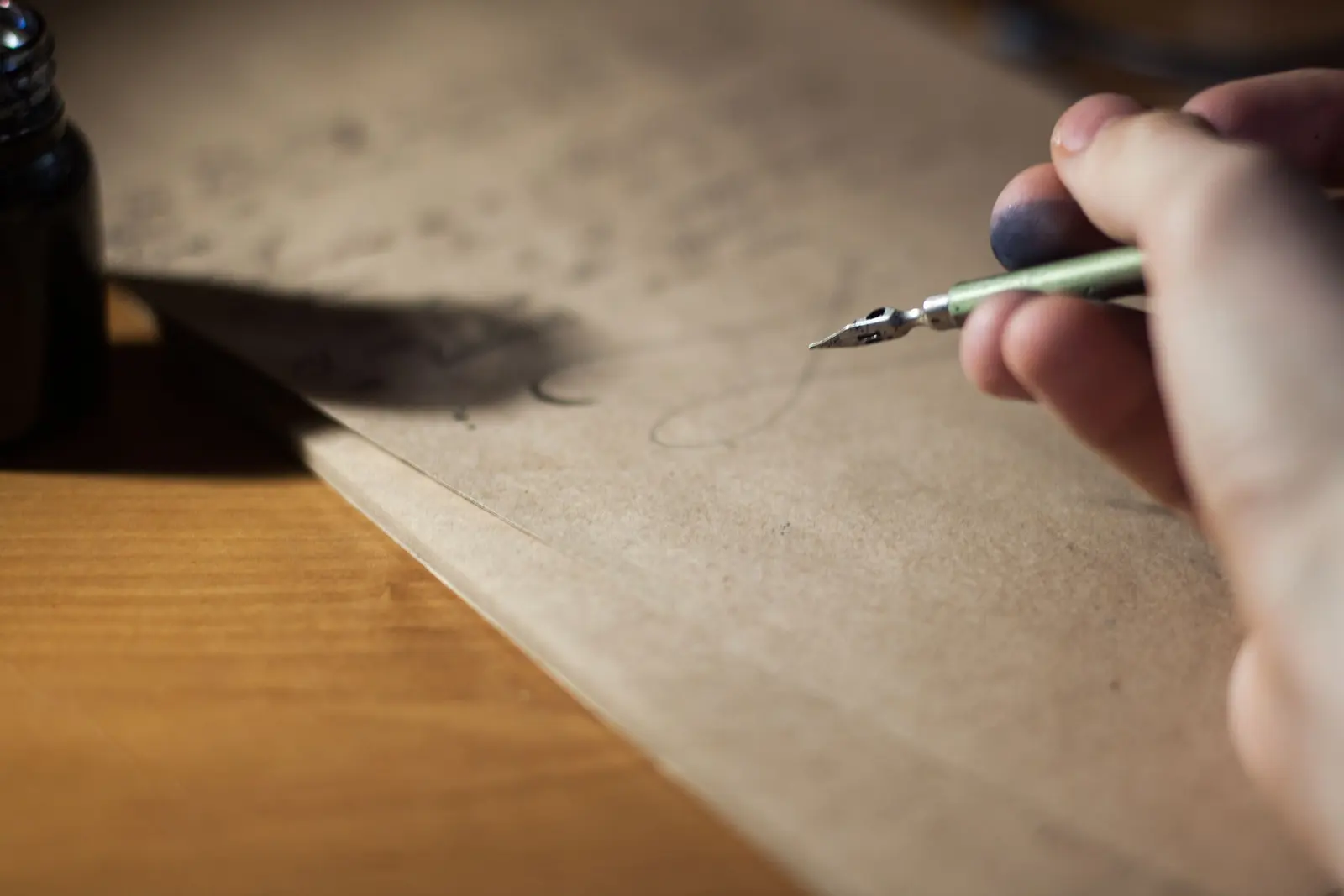 Una mano scrive con il pennino su un foglio di carta ruvida, accanto al calamaio