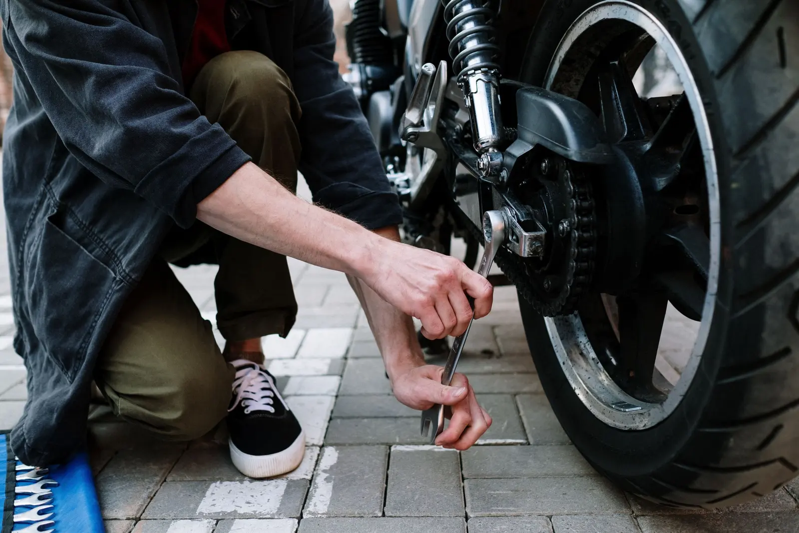 Mani con una chiave inglese sulla ruota posteriore di una moto