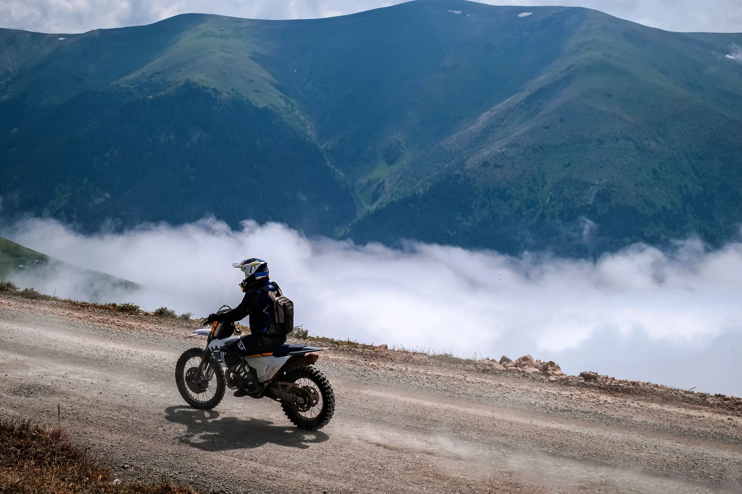 Una moto da enduro su uno sterrato di montagna, sopra un mare di nuvole