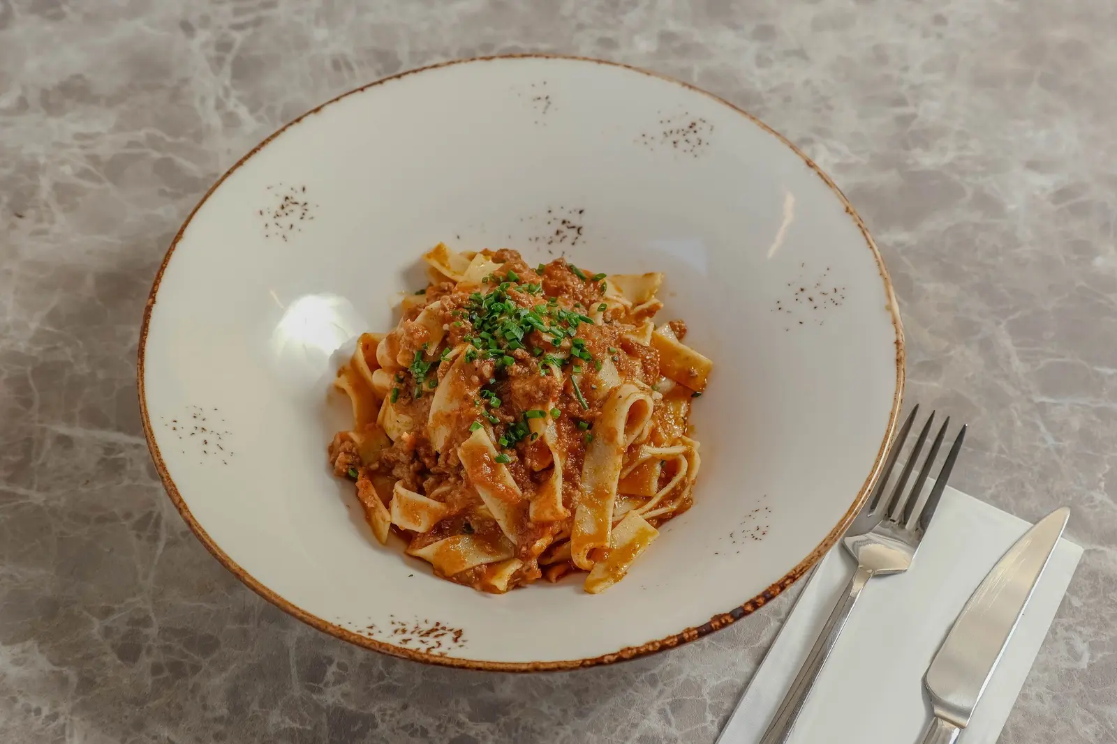 Tagliatelle al ragù in un piatto fondo bianco, con forchetta e coltello