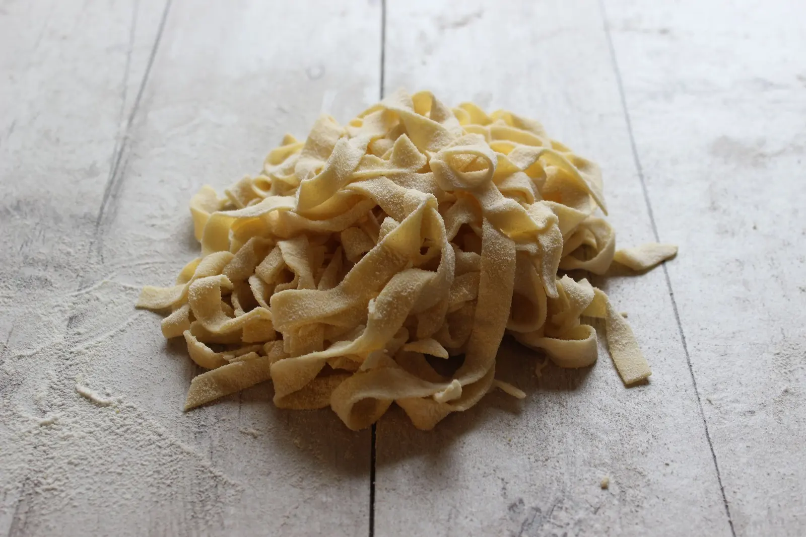 Un mucchio di tagliatelle appena tagliate su un tavolo di legno chiaro