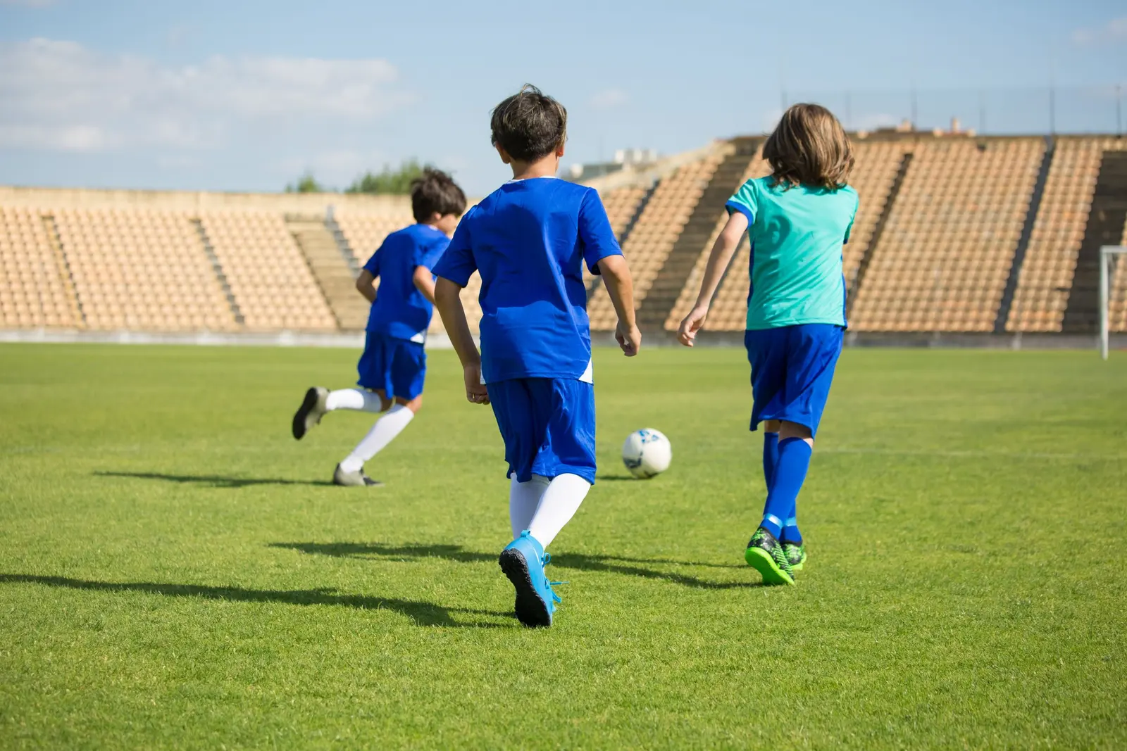 Tre bambini visti di spalle che inseguono il pallone sul campo
