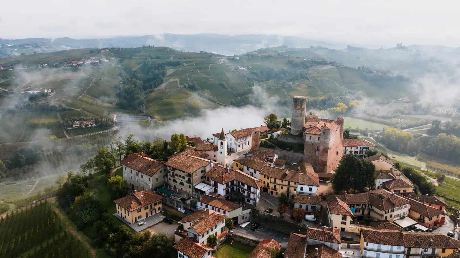 Borgo con castello sulla collina tra la nebbia, vigneti intorno