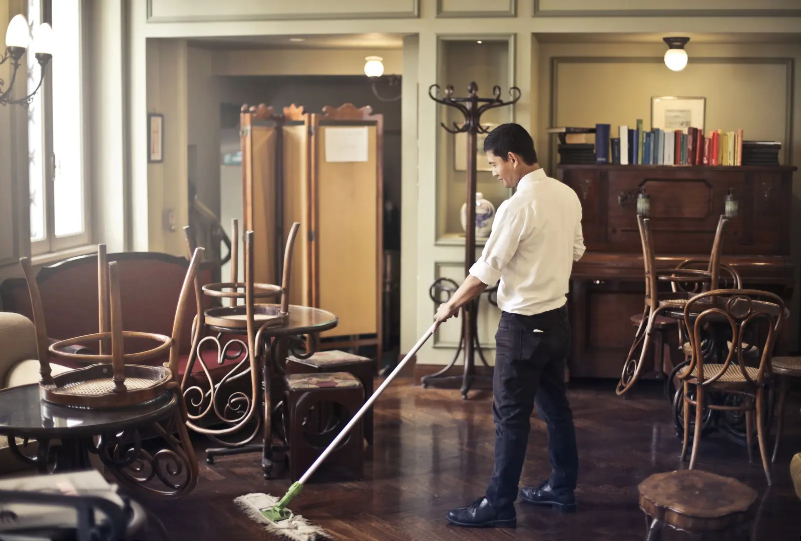 Un cameriere lava il parquet della sala con il mocio, con le sedie capovolte sui tavoli