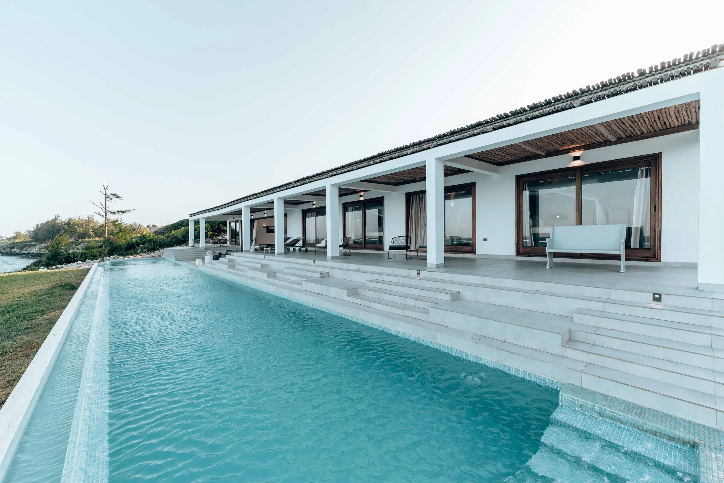 Casa bianca bassa sul mare: portico a pilastri con pergolato in canne e una lunga piscina davanti