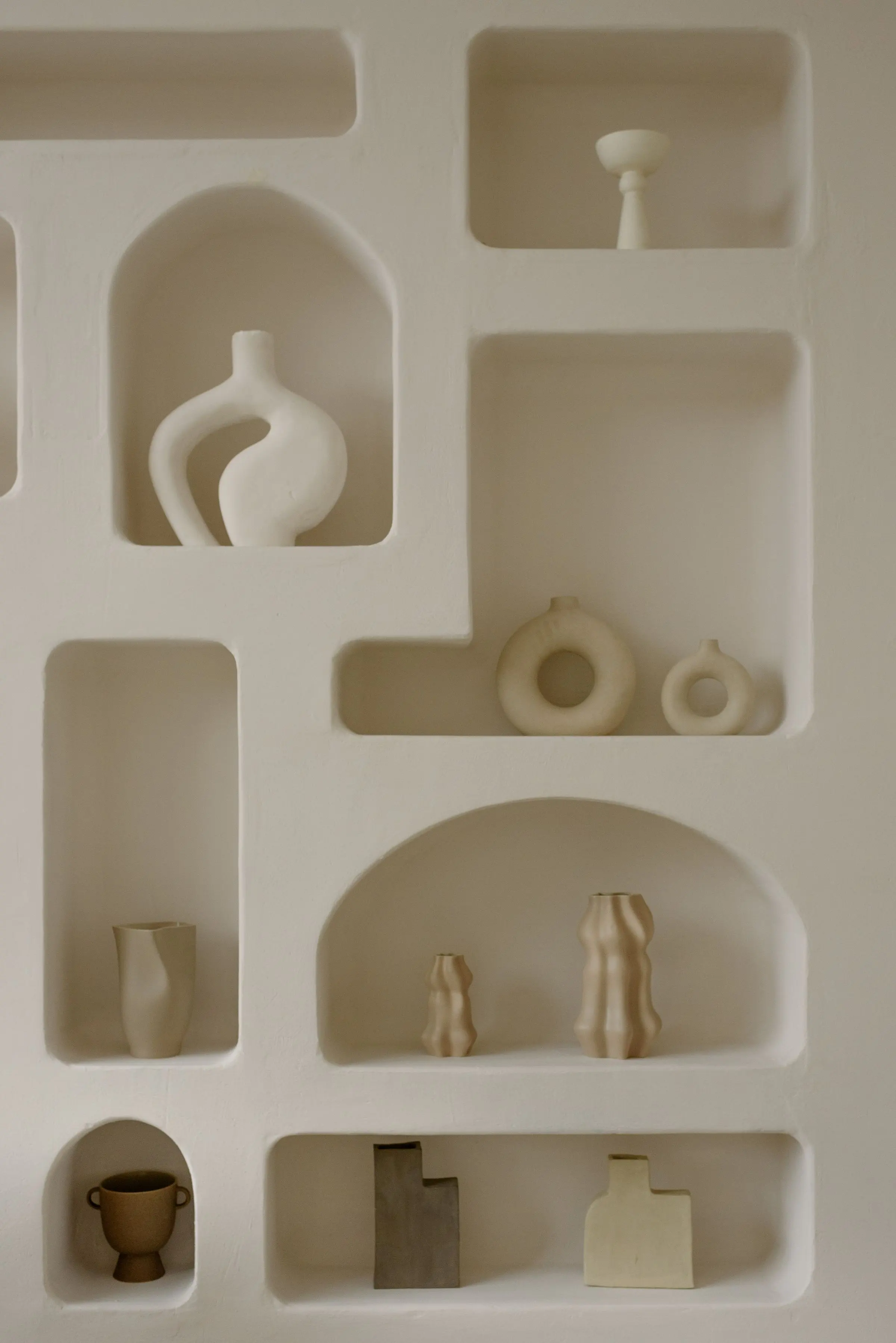 Parete bianca con nicchie di forme diverse scavate nell'intonaco, con vasi e ceramiche chiare