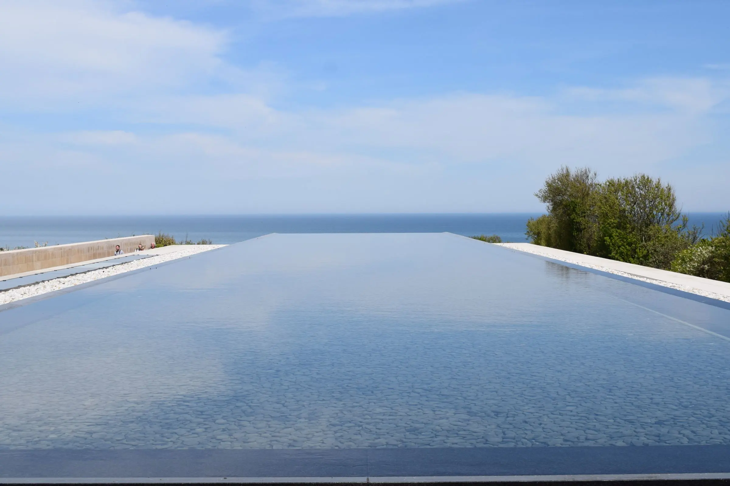 Piscina a sfioro con il bordo allineato all'orizzonte del mare, sotto un cielo con nuvole leggere