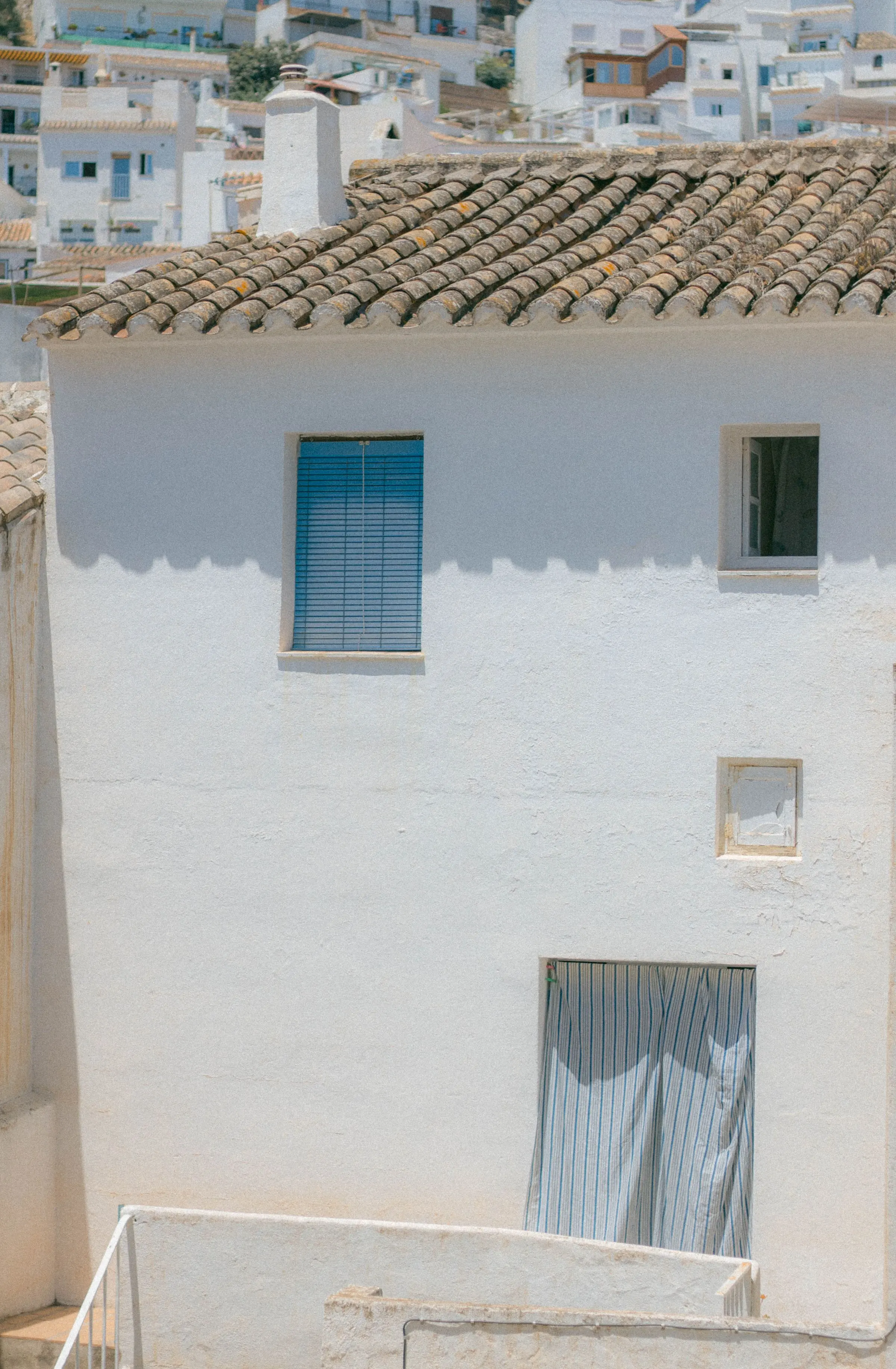Facciata bianca a calce di una casa su più piani, con tetto in coppi e una persiana azzurra