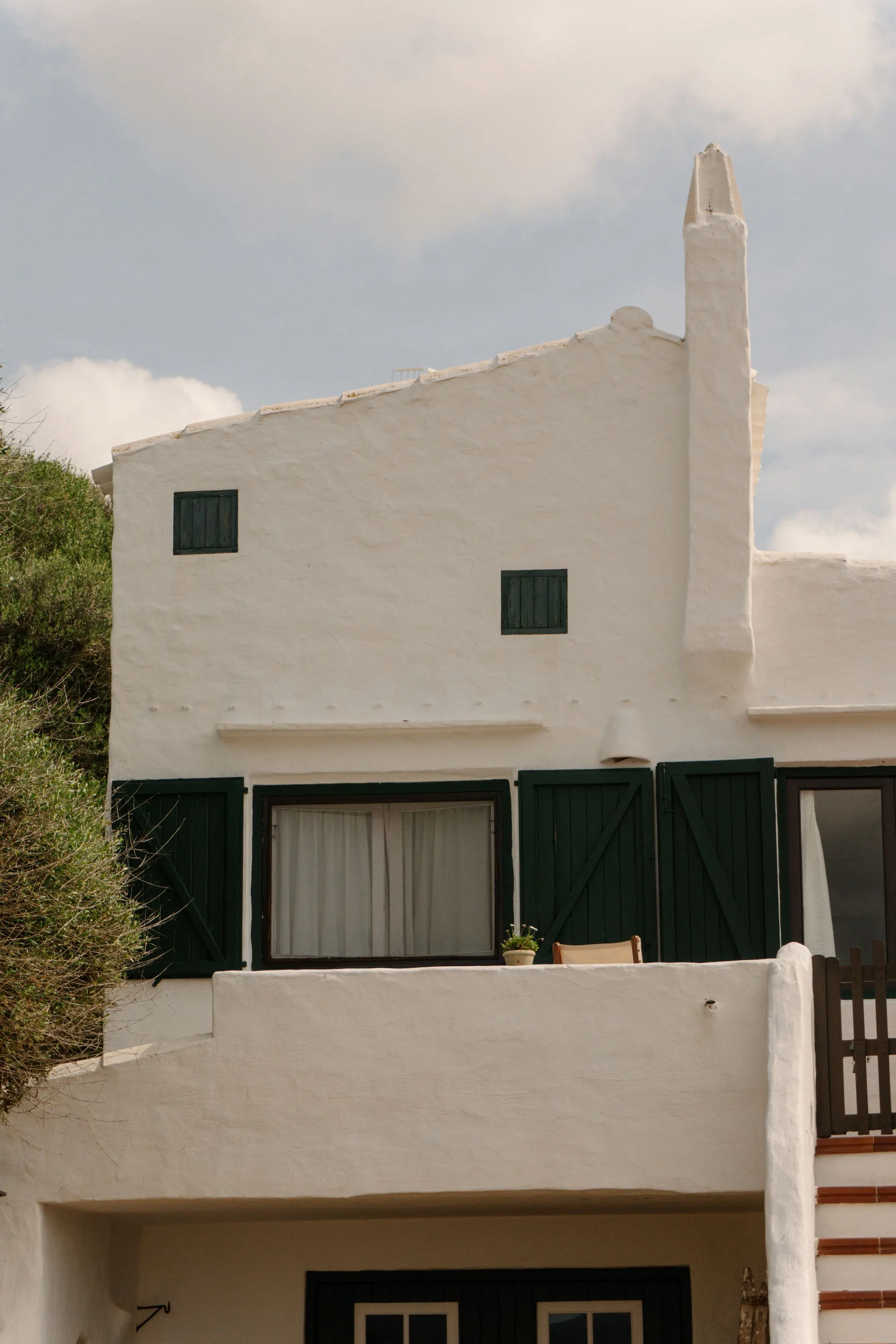Casa bianca intonacata con persiane verdi, un comignolo alto e la macchia mediterranea accanto