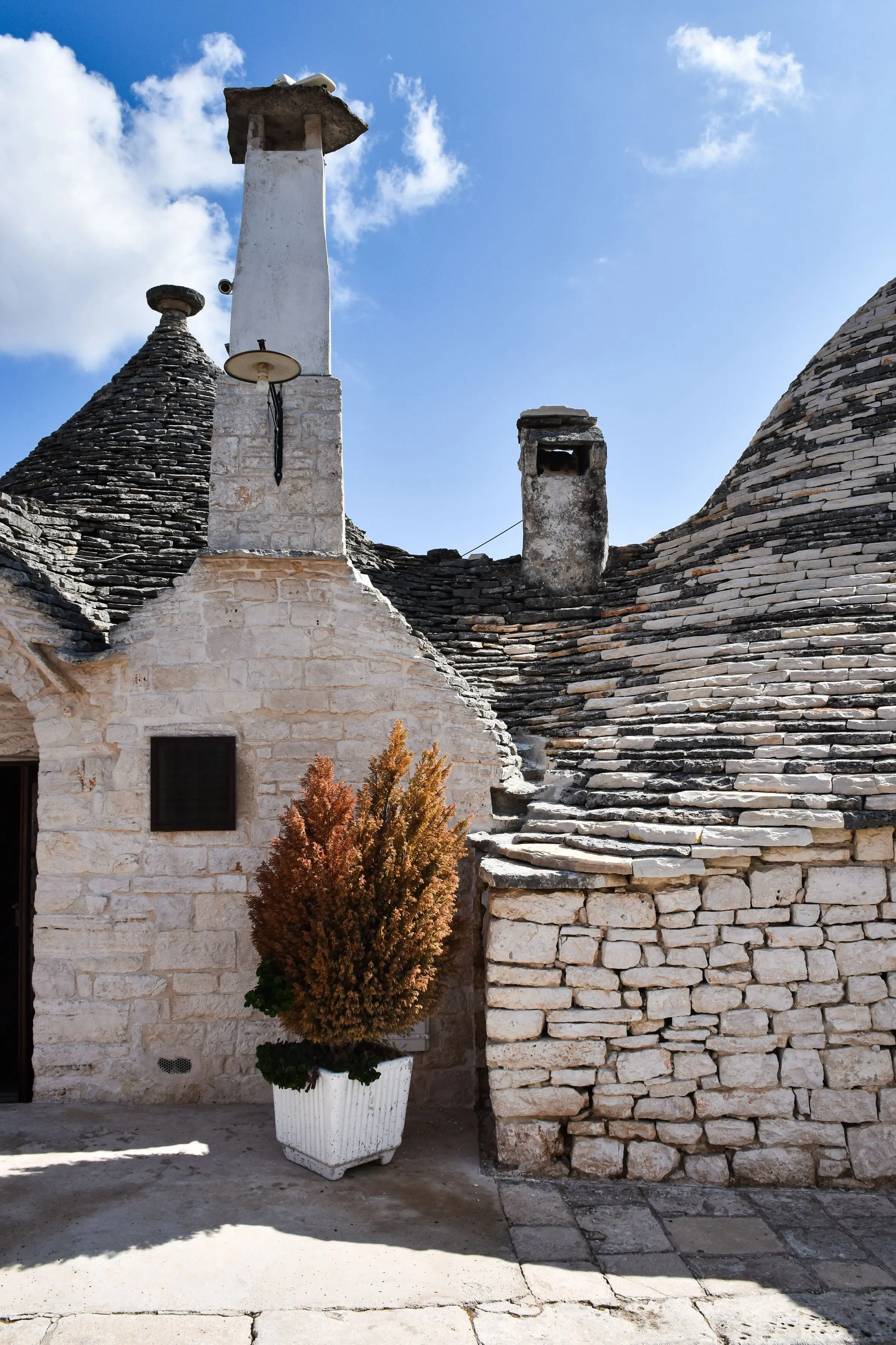 Trulli con i coni in pietra a secco, comignoli bianchi e un muretto in pietra