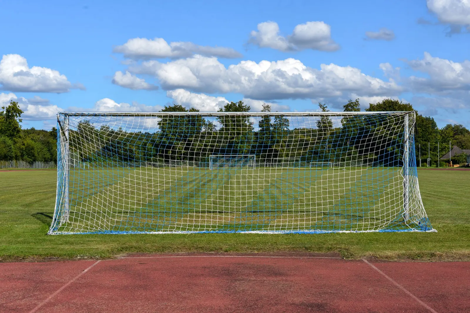 Porta da calcio a 11 bianca su un prato, dietro la pista d'atletica rossa