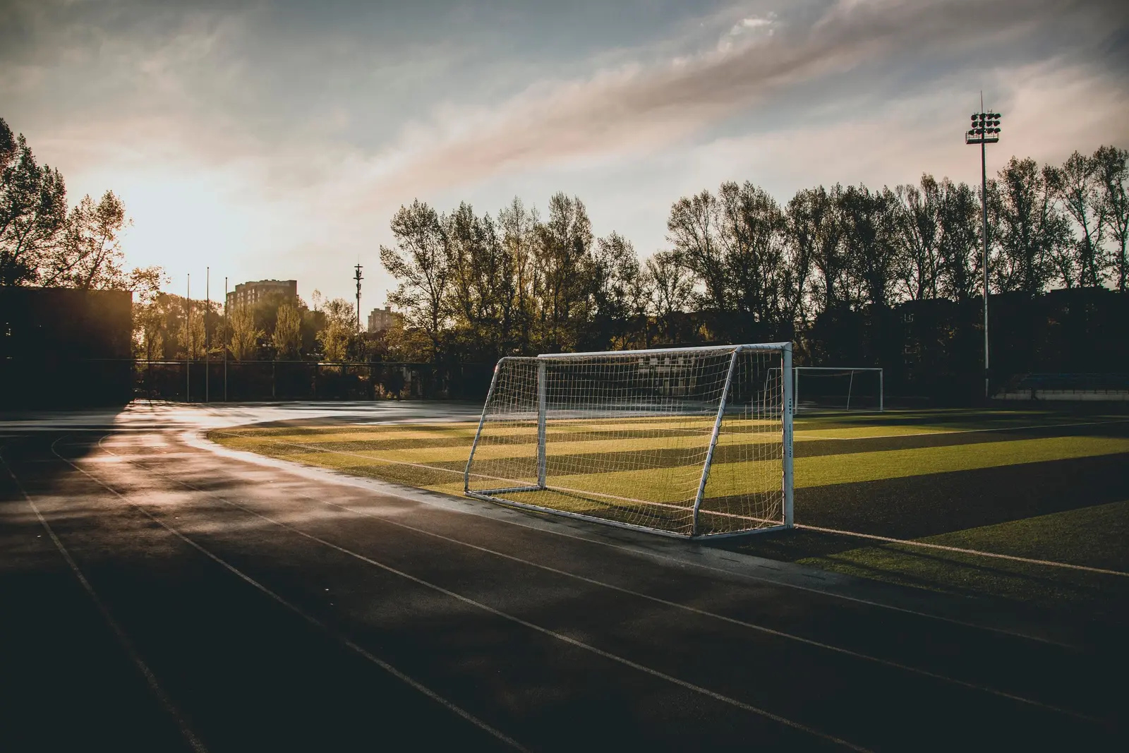 Porta da calcio su un campo comunale al tramonto, con la pista d'atletica in primo piano