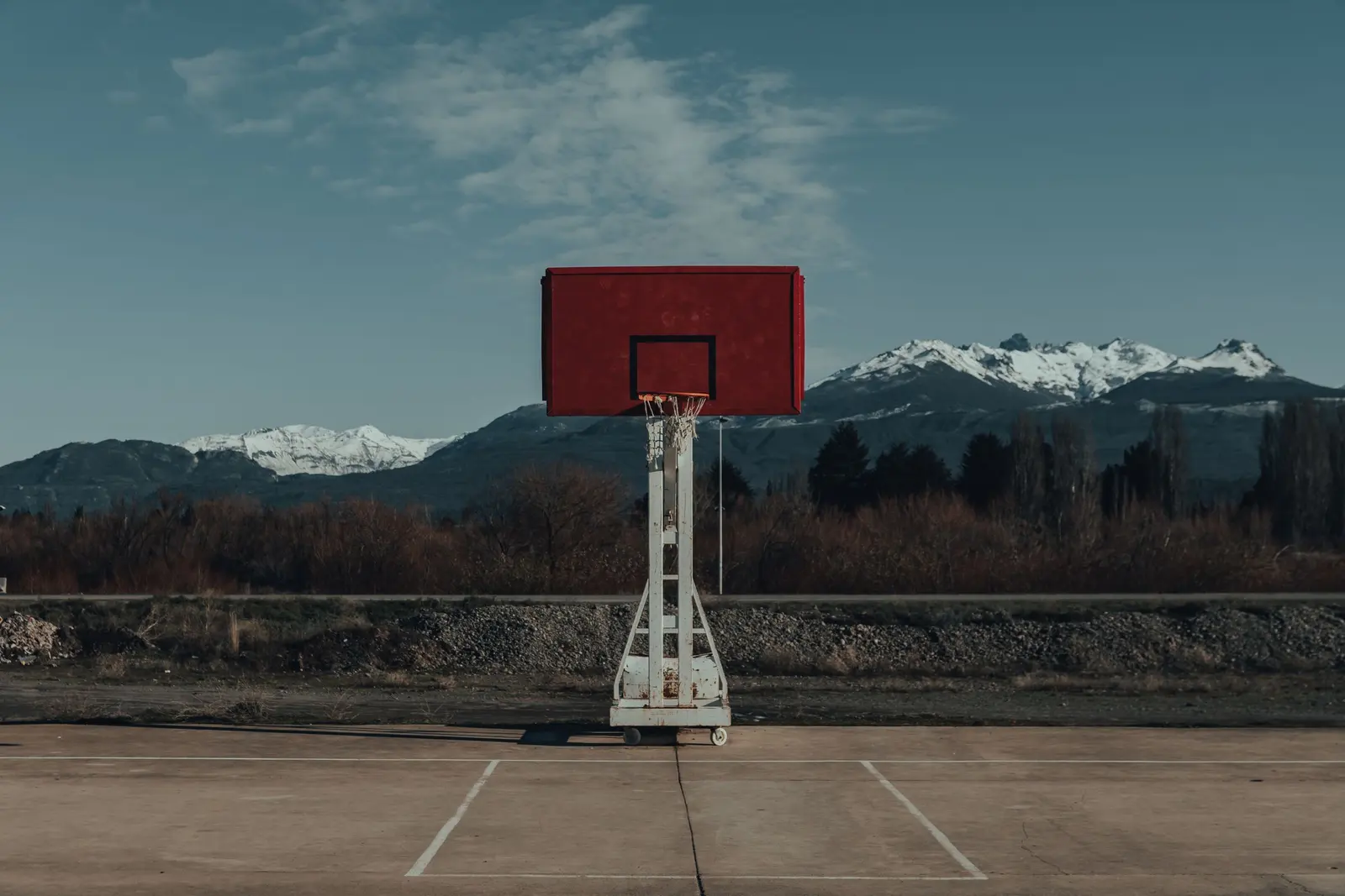 Impianto basket rosso e bianco su una piastra all'aperto, con le montagne innevate sullo sfondo