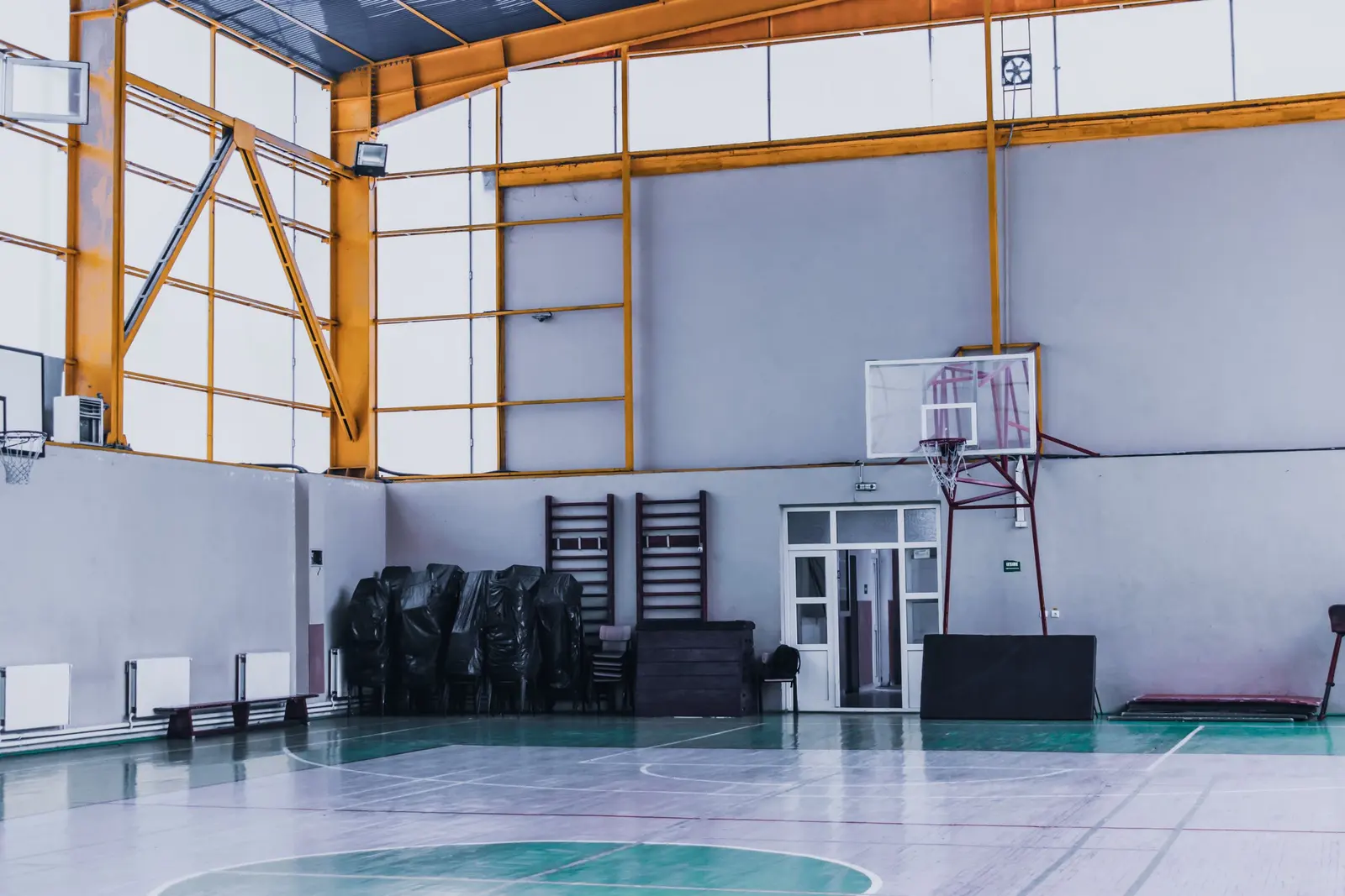 Palestra scolastica con impianto basket a parete, spalliere e pavimento verde