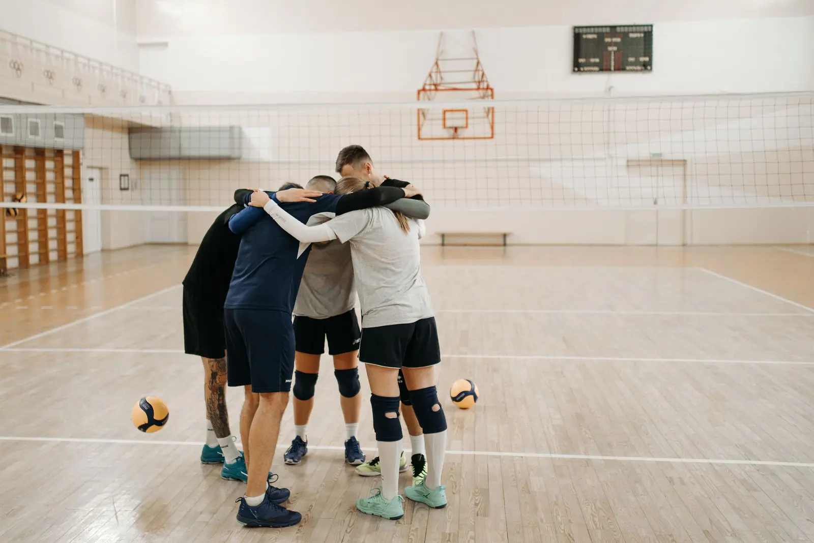 Squadra di pallavolo abbracciata in cerchio al centro della palestra, palloni a terra