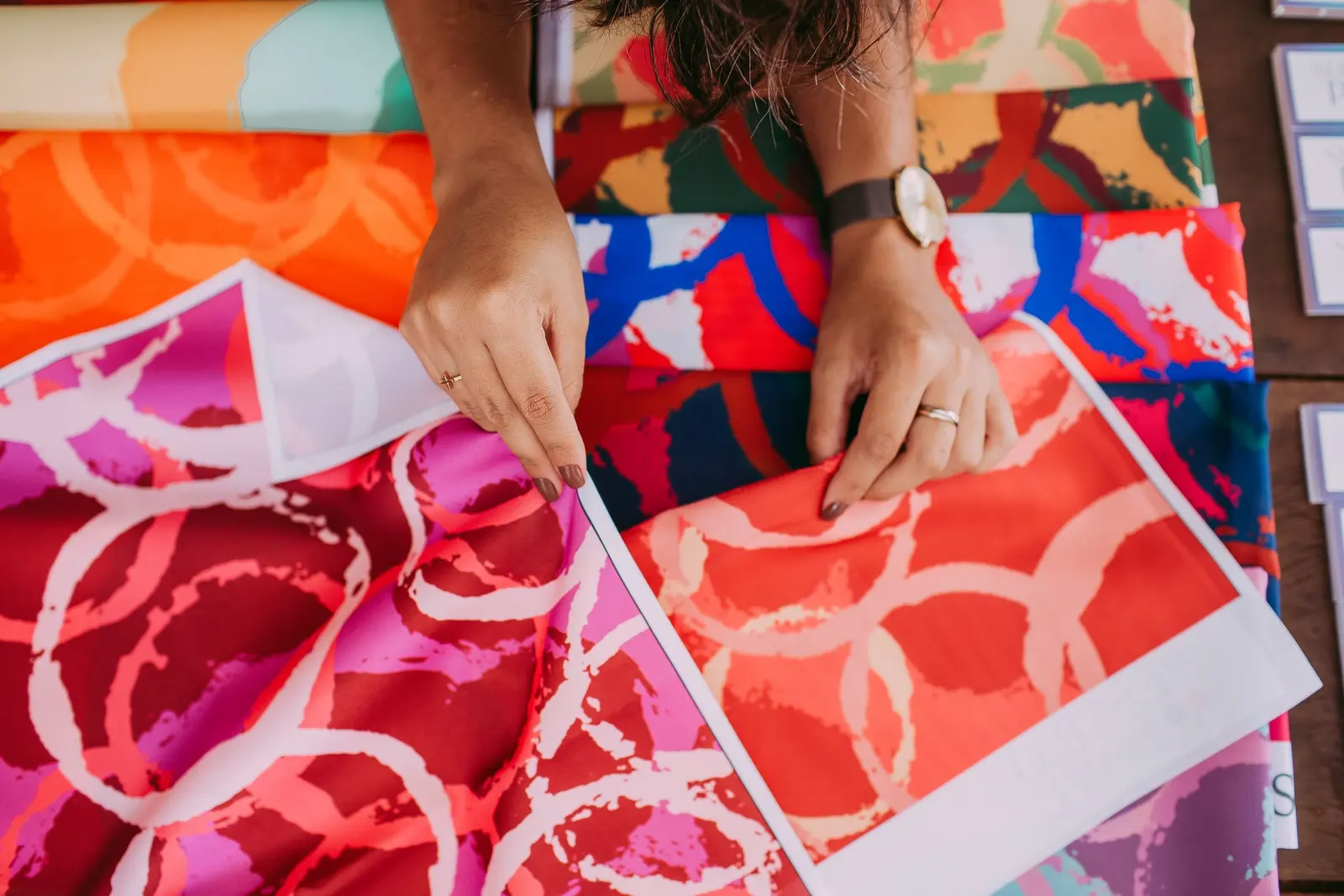 Mani che sistemano campioni di tessuto stampato a fantasie rosse, arancioni e rosa