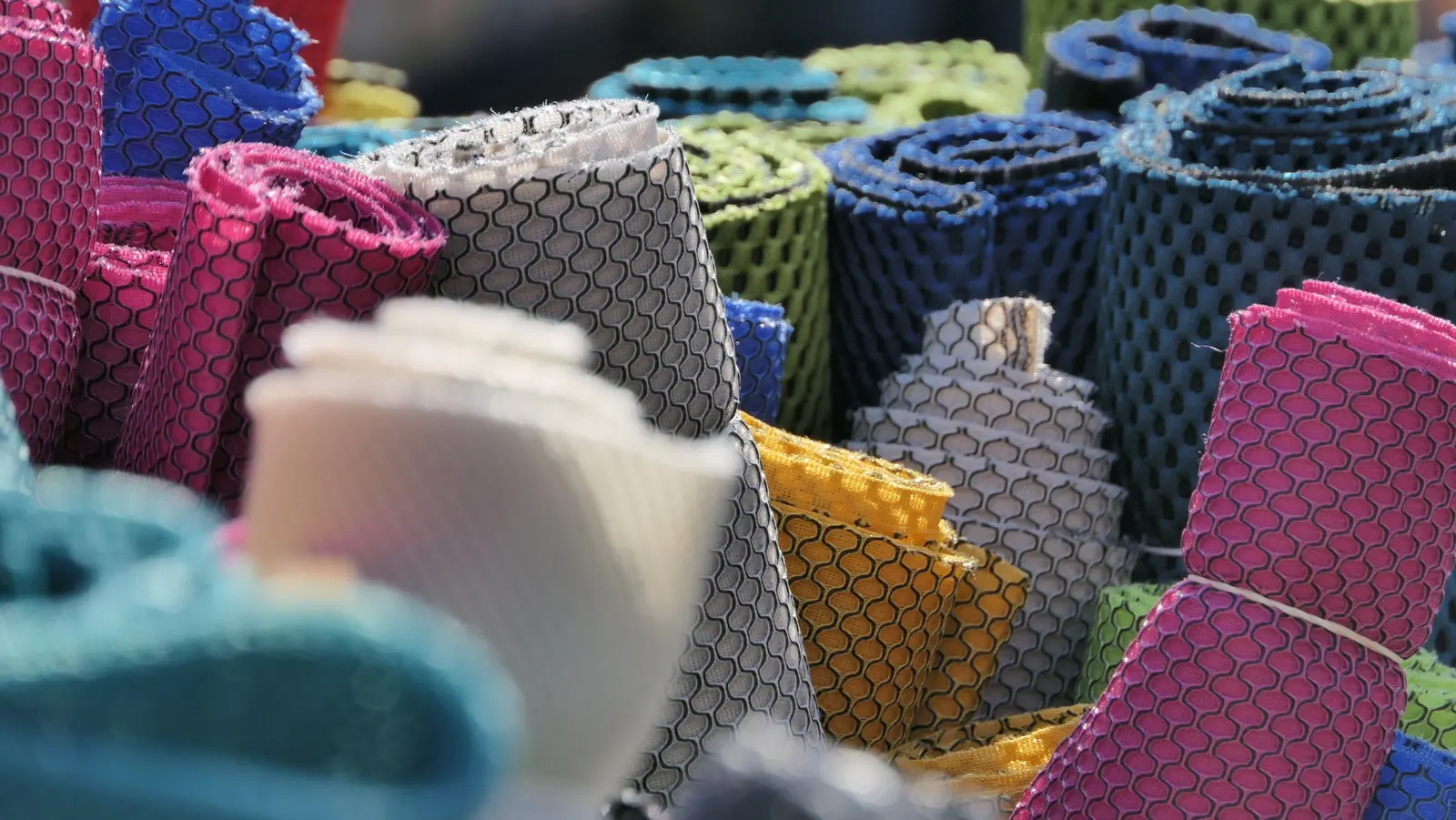 Rotoli di tessuto a rete traforata in tanti colori: rosa, grigio, blu, giallo, verde acqua