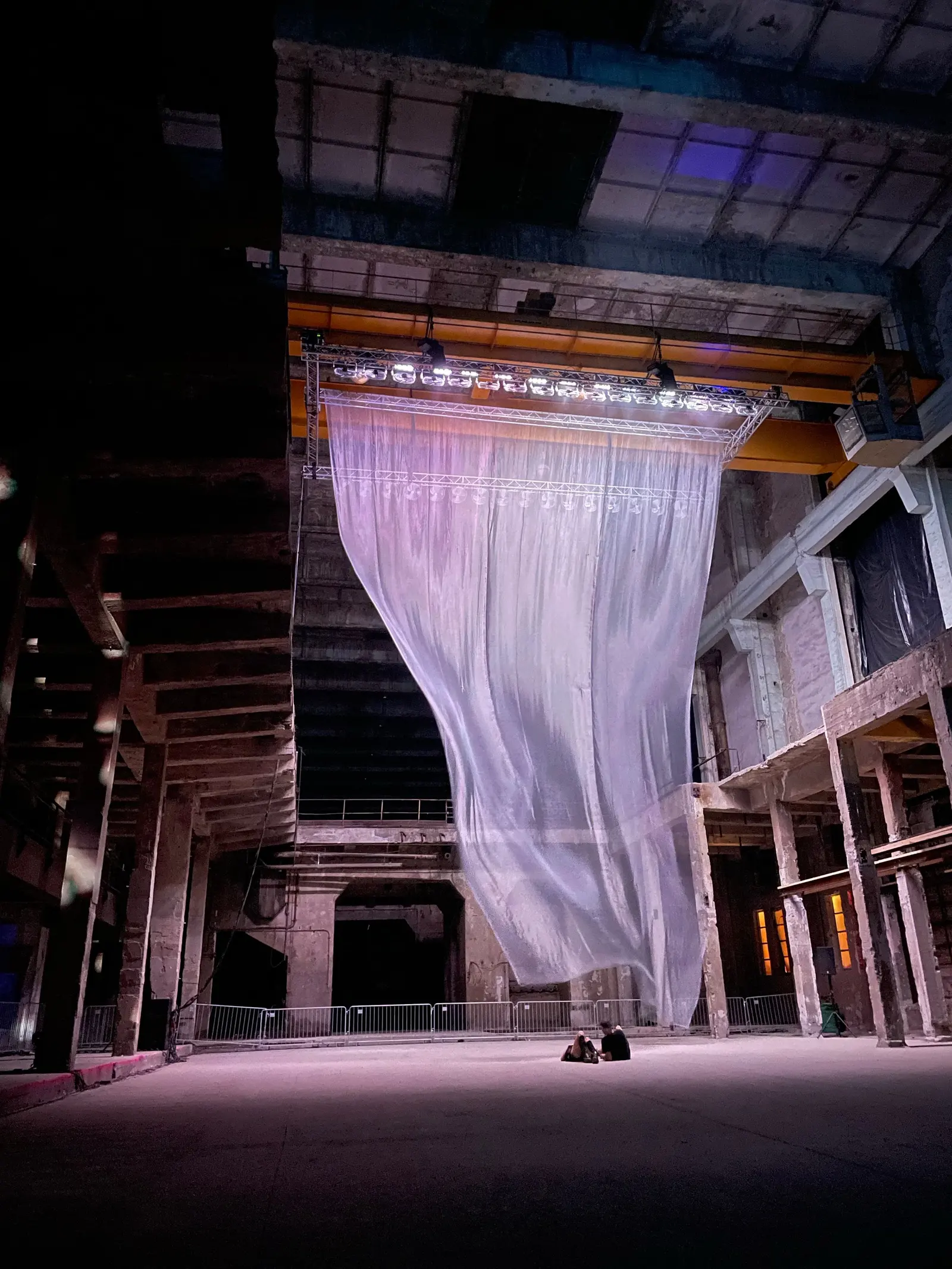 Un'ex centrale industriale in penombra: un grande telo bianco trasparente scende da un'americana illuminata