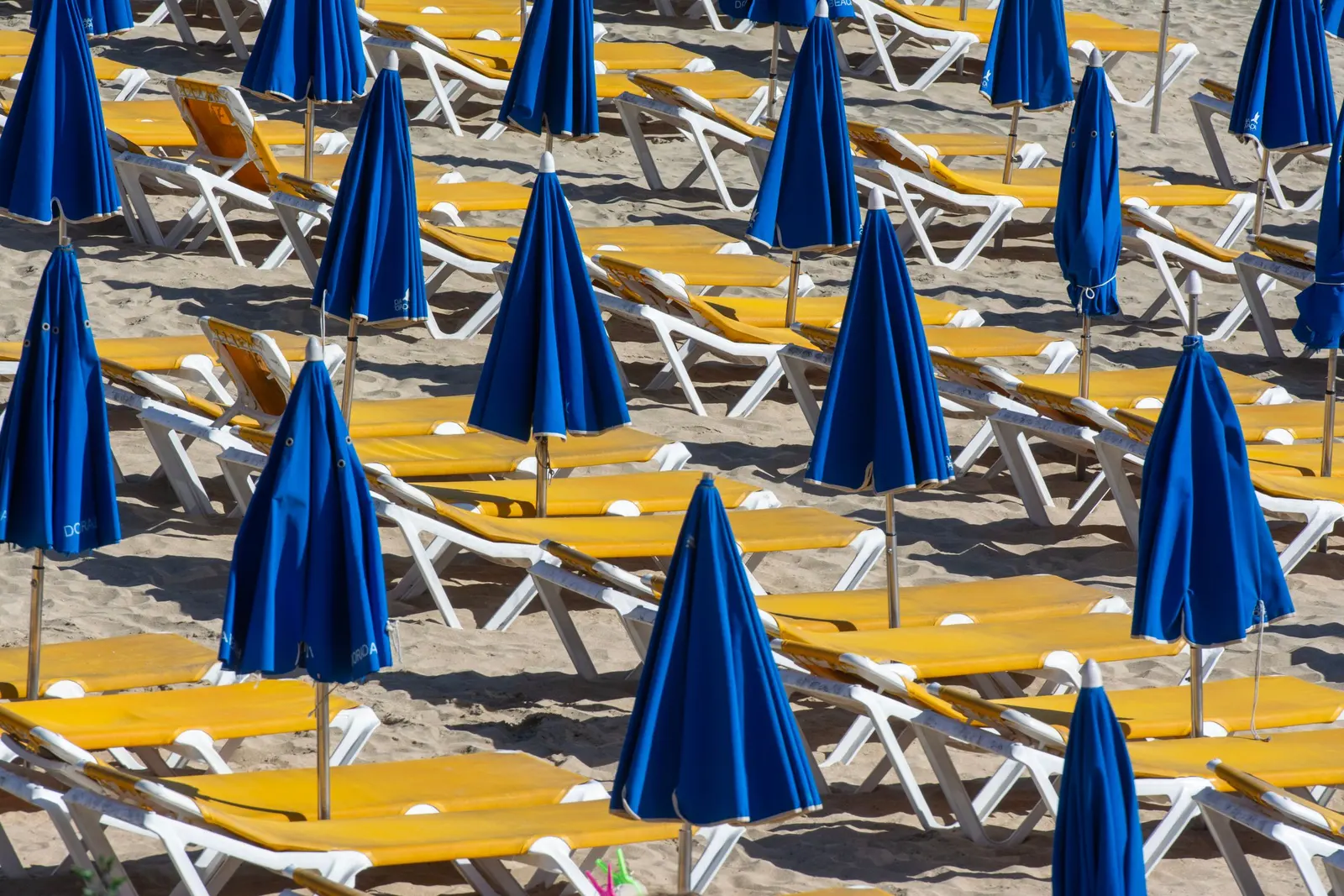 Ombrelloni blu chiusi e lettini gialli allineati sulla sabbia