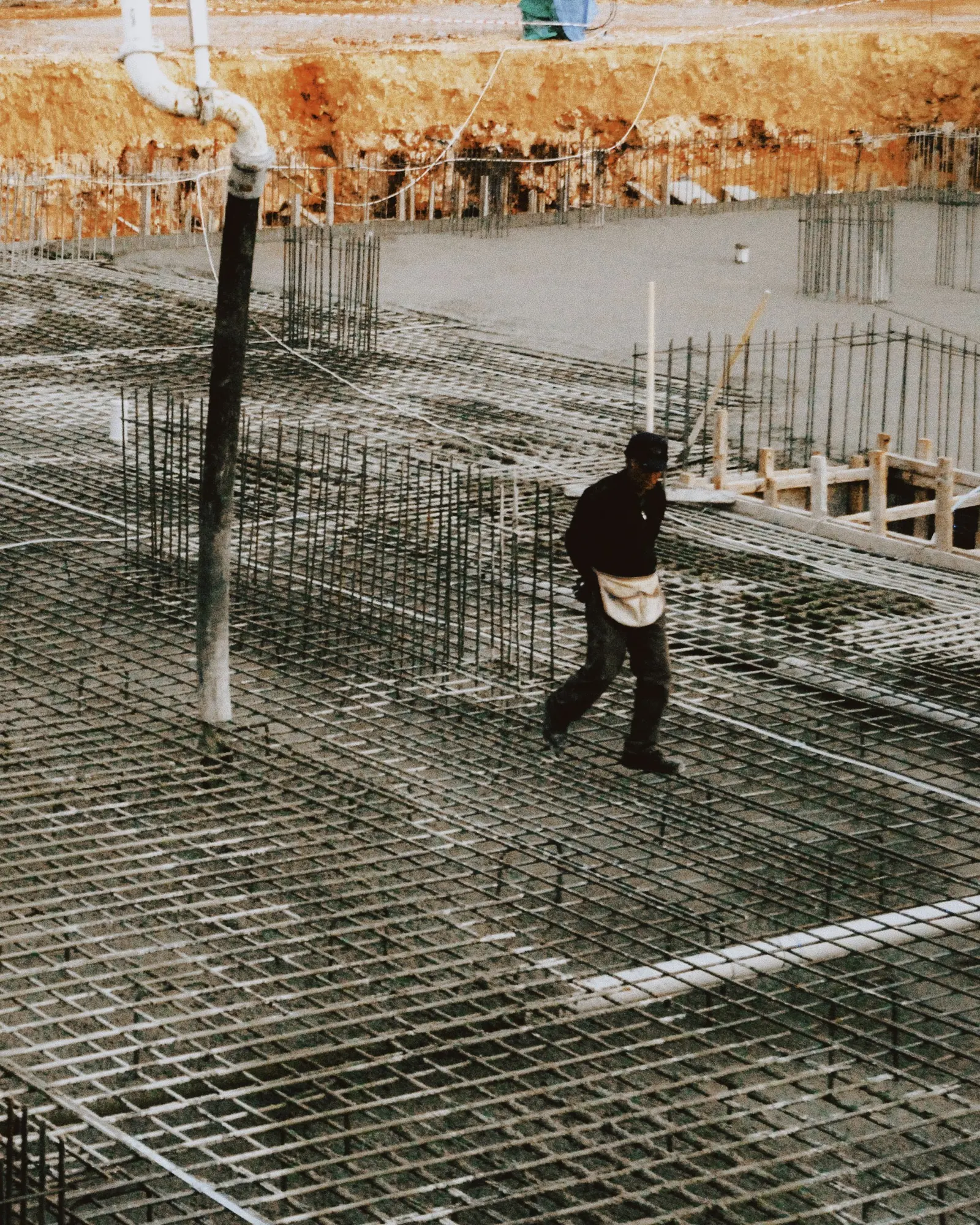Rete d'armatura stesa sul terreno prima del getto, un operaio la attraversa