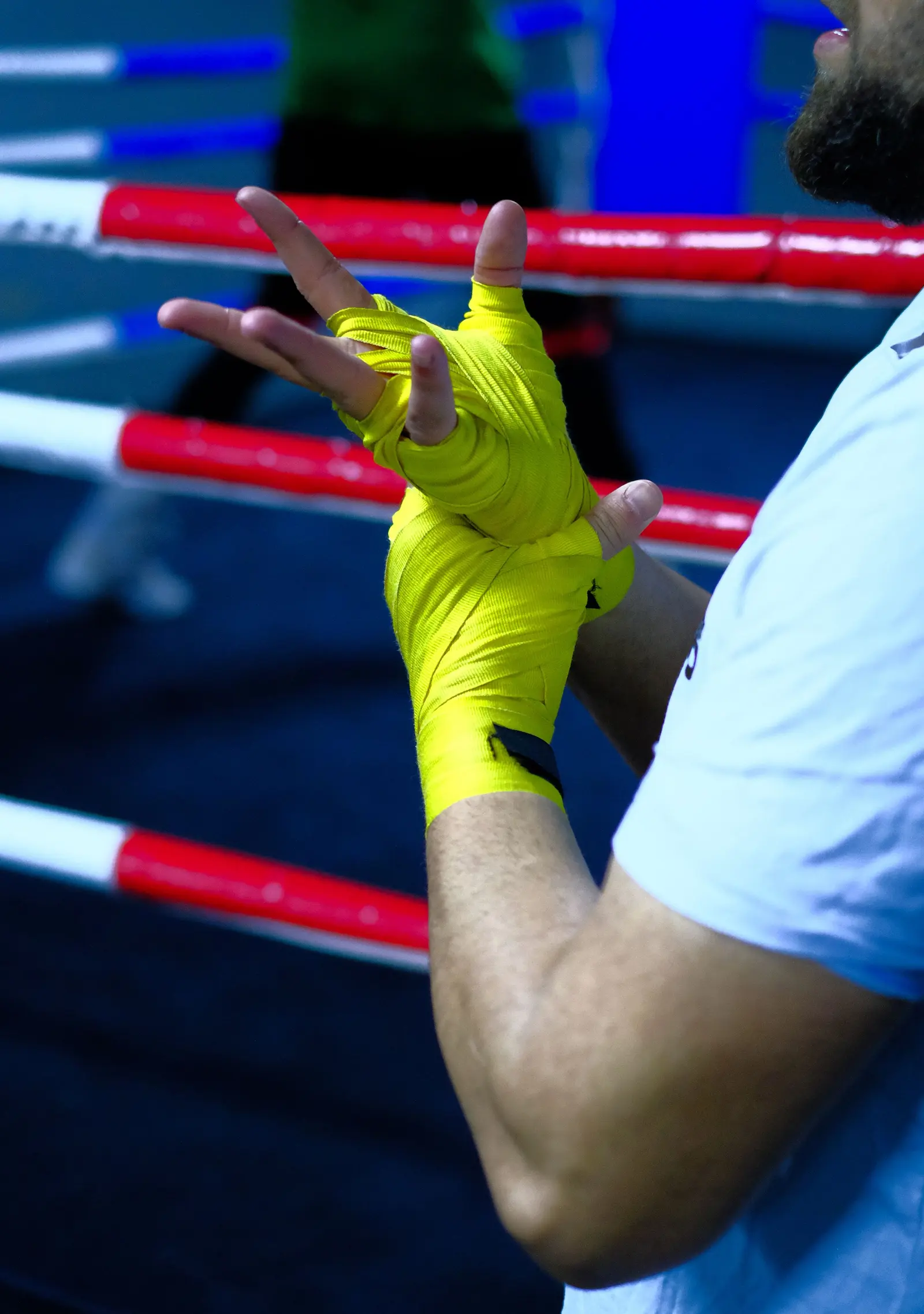 Una mano fasciata con bende giallo acido, con le corde del ring dietro