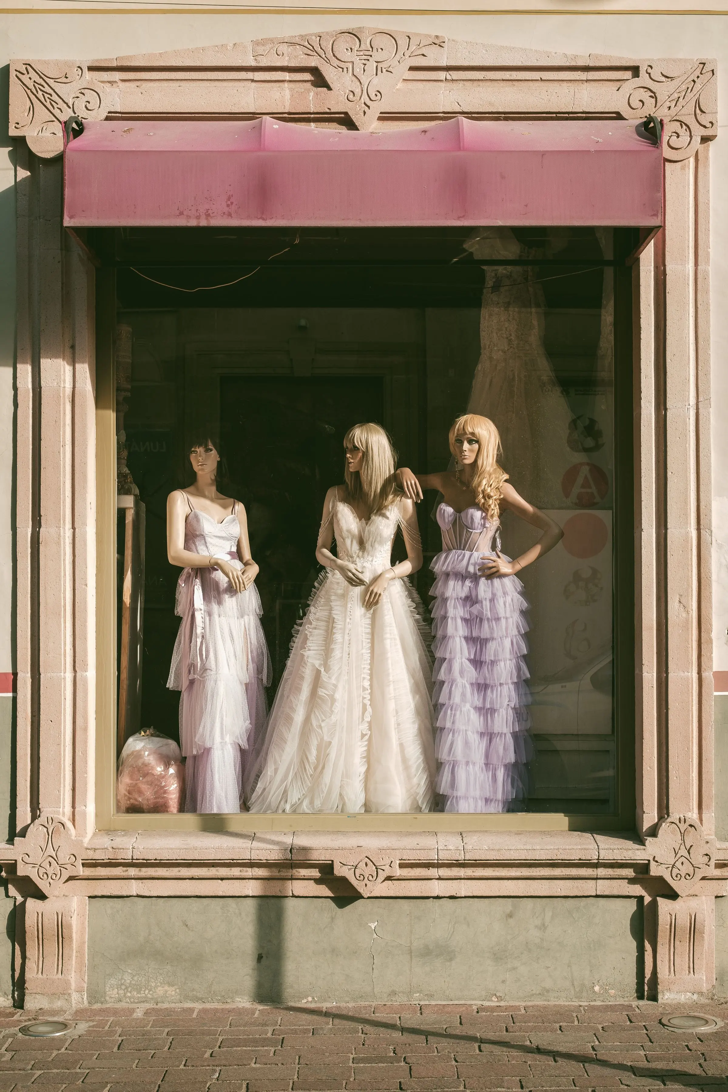 Tre abiti da sposa in una vetrina con cornice di pietra rosa e una tenda
