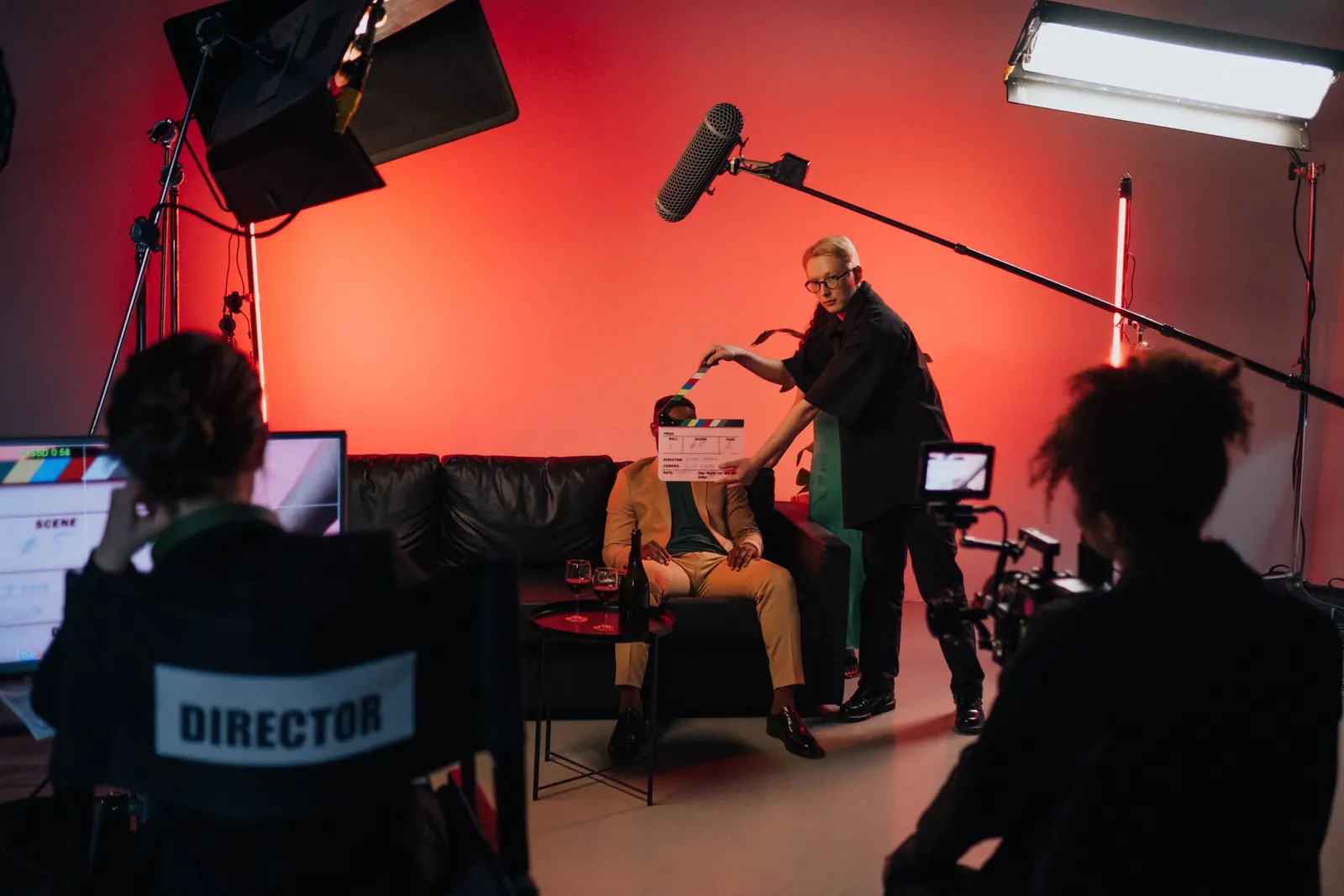 Un set in studio con luce rossa: il regista, la claquette, il microfono sull'asta e i monitor