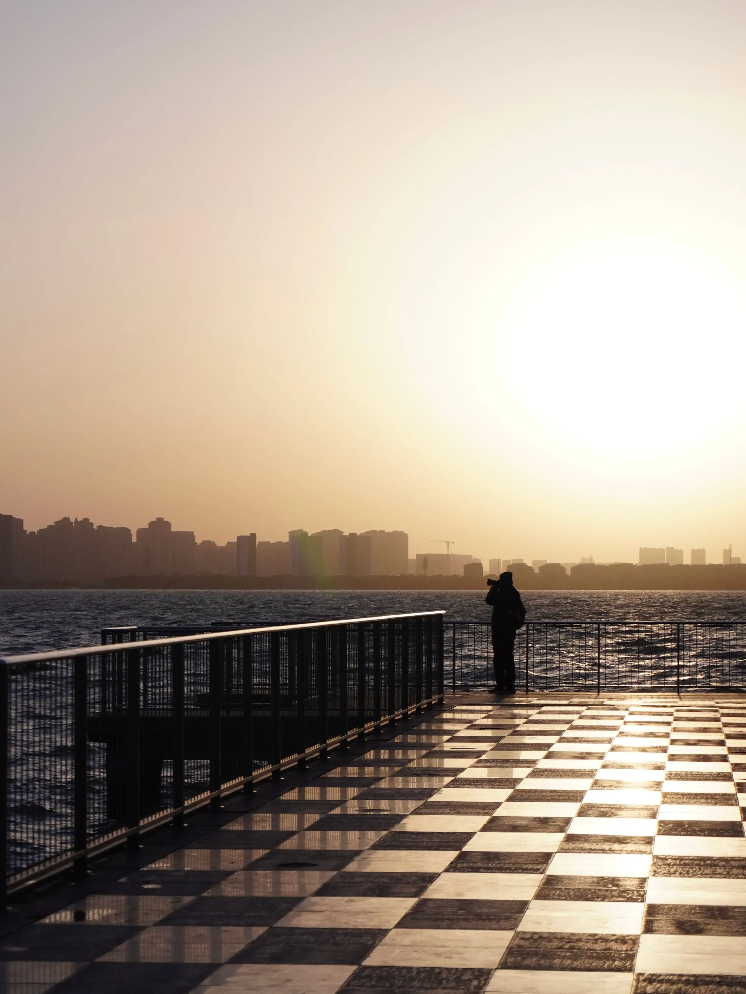 Un molo sul mare al tramonto, pavimento a scacchi e una persona sola in fondo