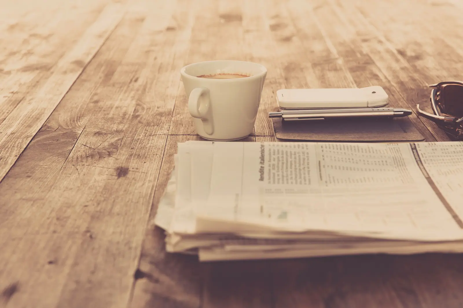Una tazza di caffè, un telefono e i giornali piegati su un tavolo di legno