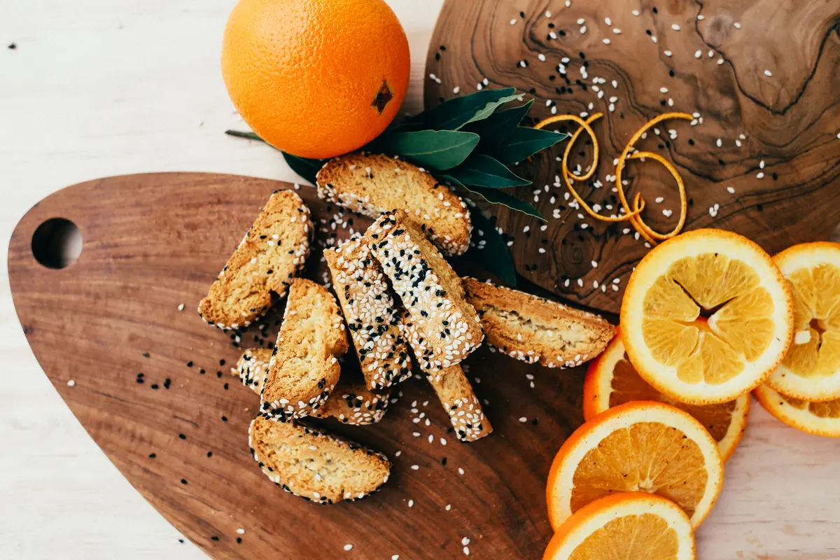Tozzetti al sesamo su un tagliere di legno, accanto a fette d'arancia