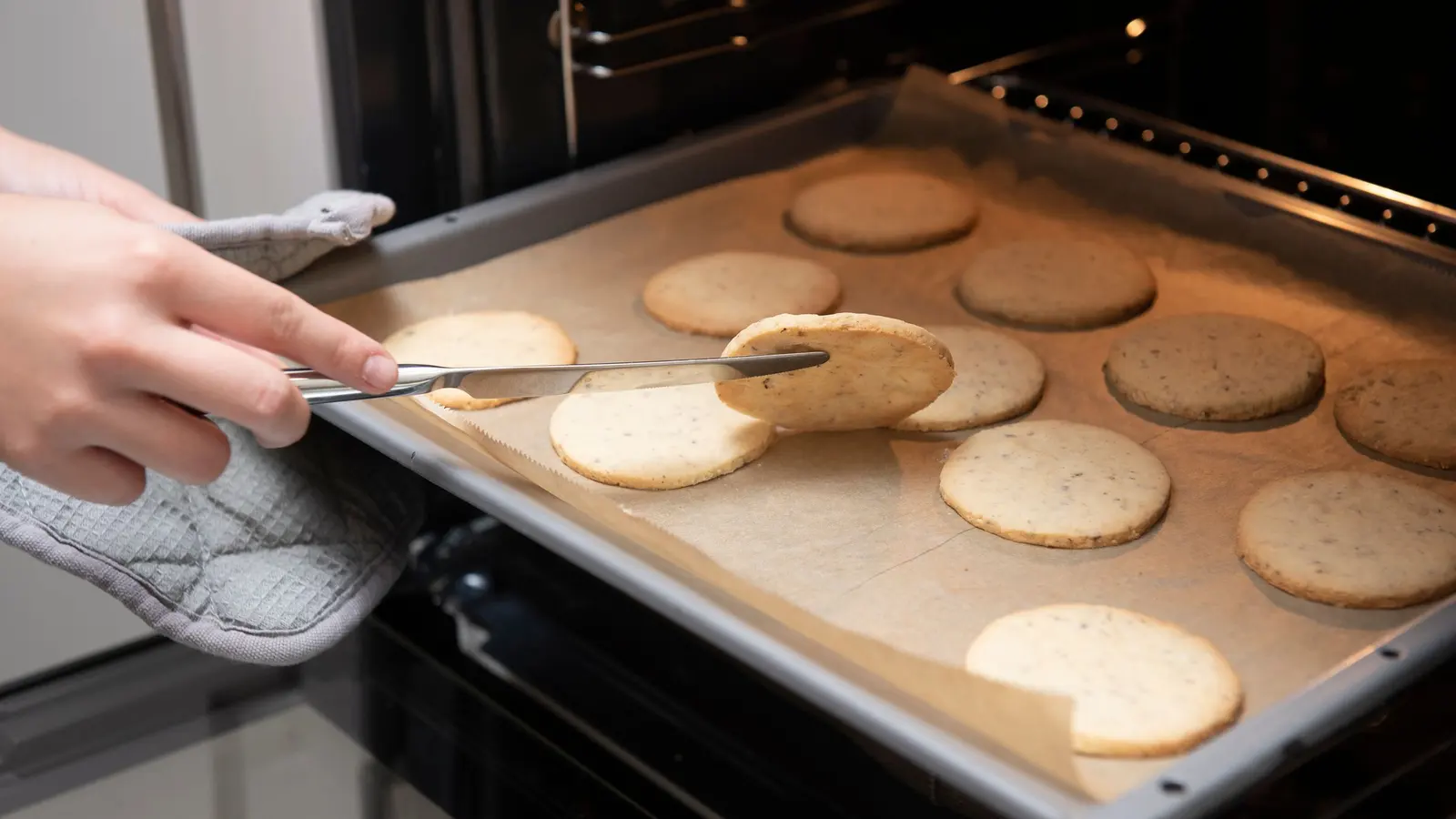 Una teglia di frollini tondi appena tolta dal forno, una mano con il guanto