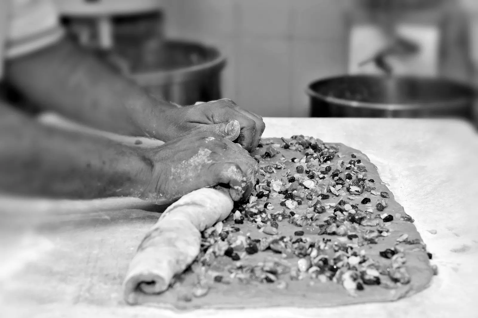 Mani che arrotolano un impasto con frutta secca sul banco, in bianco e nero
