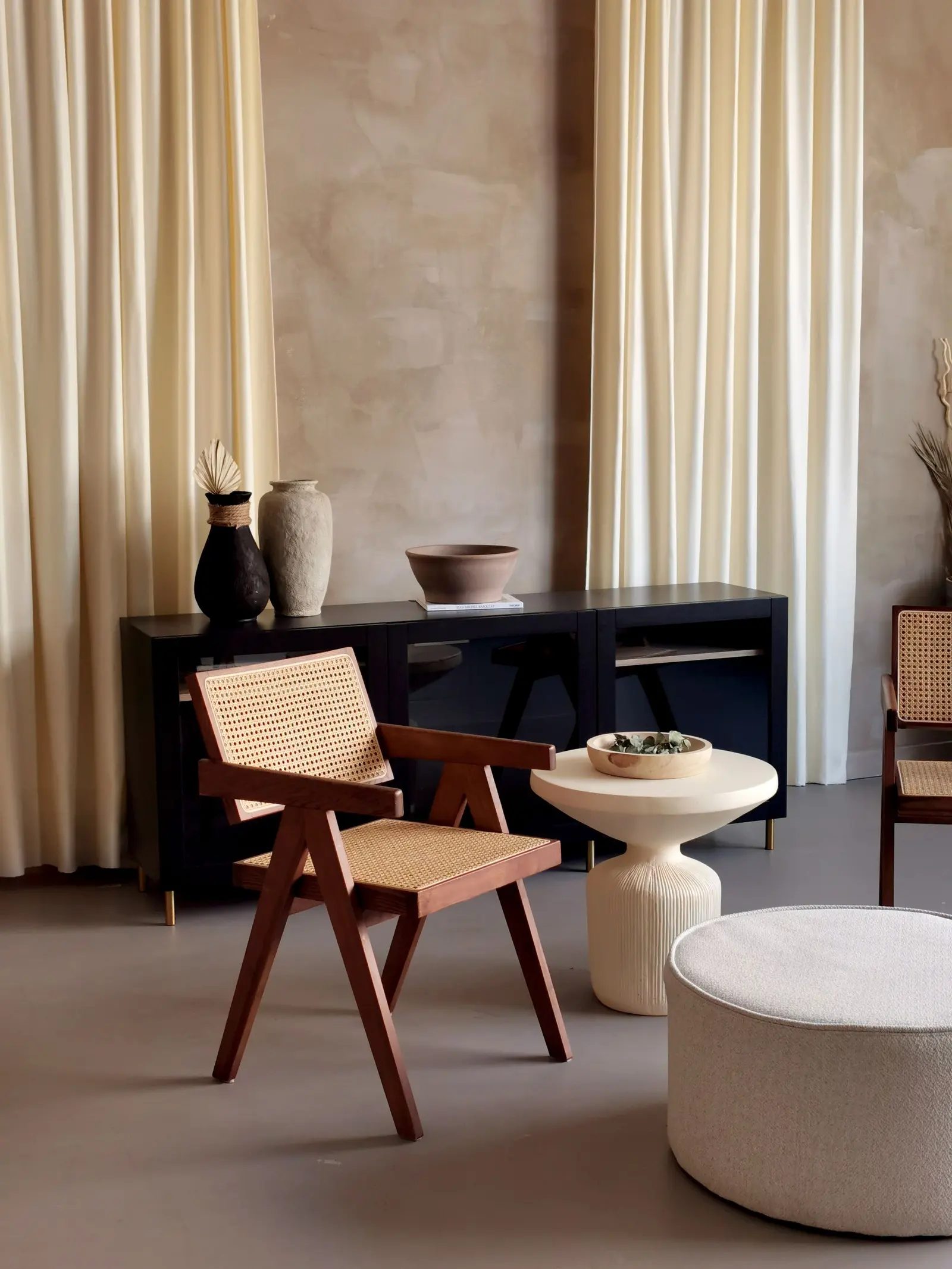Angolo dello showroom: parete in calce, pavimento continuo grigio, una sedia in legno e canna e una credenza nera