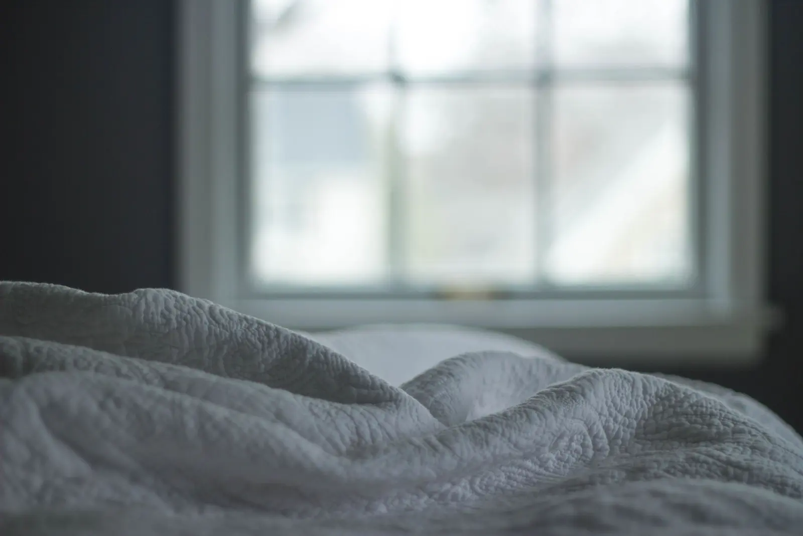 Letto con un copriletto bianco trapuntato davanti a una finestra, nella luce del mattino
