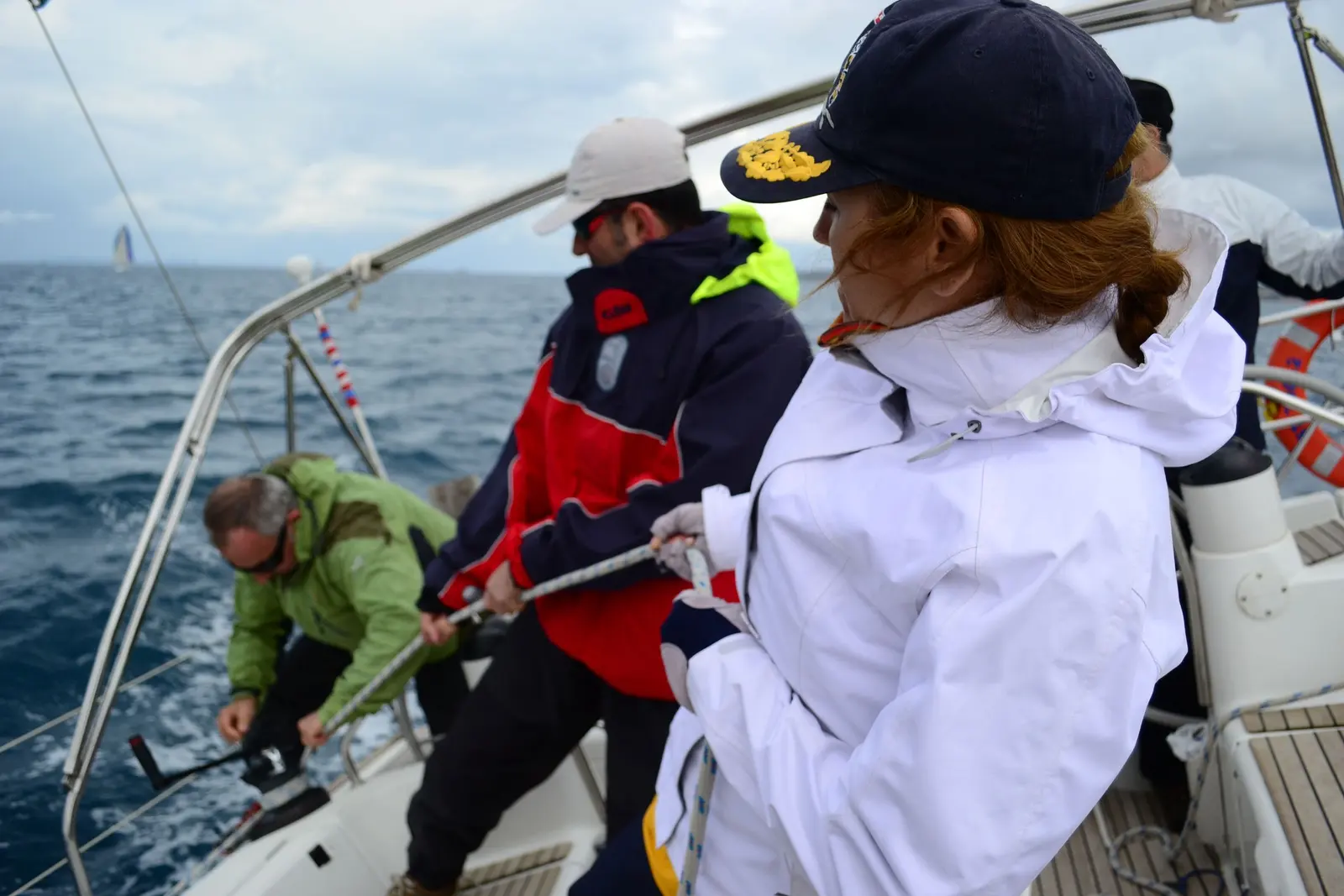 Equipaggio in cerata che cazza una scotta al winch con la barca sbandata e il mare mosso