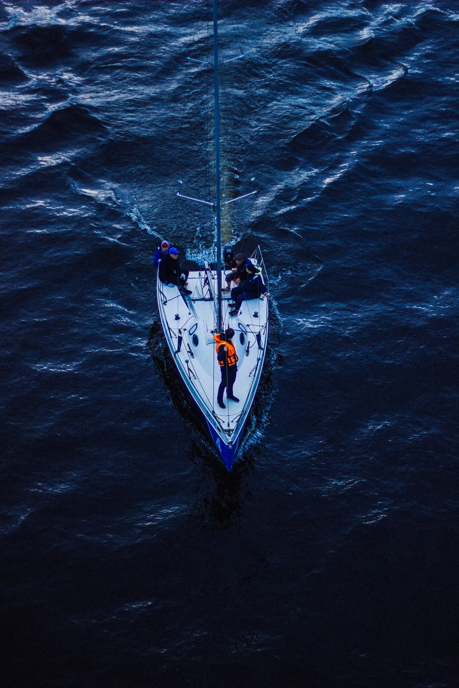 Barca a vela vista dall'alto mentre naviga sul mare blu scuro, con due persone in coperta