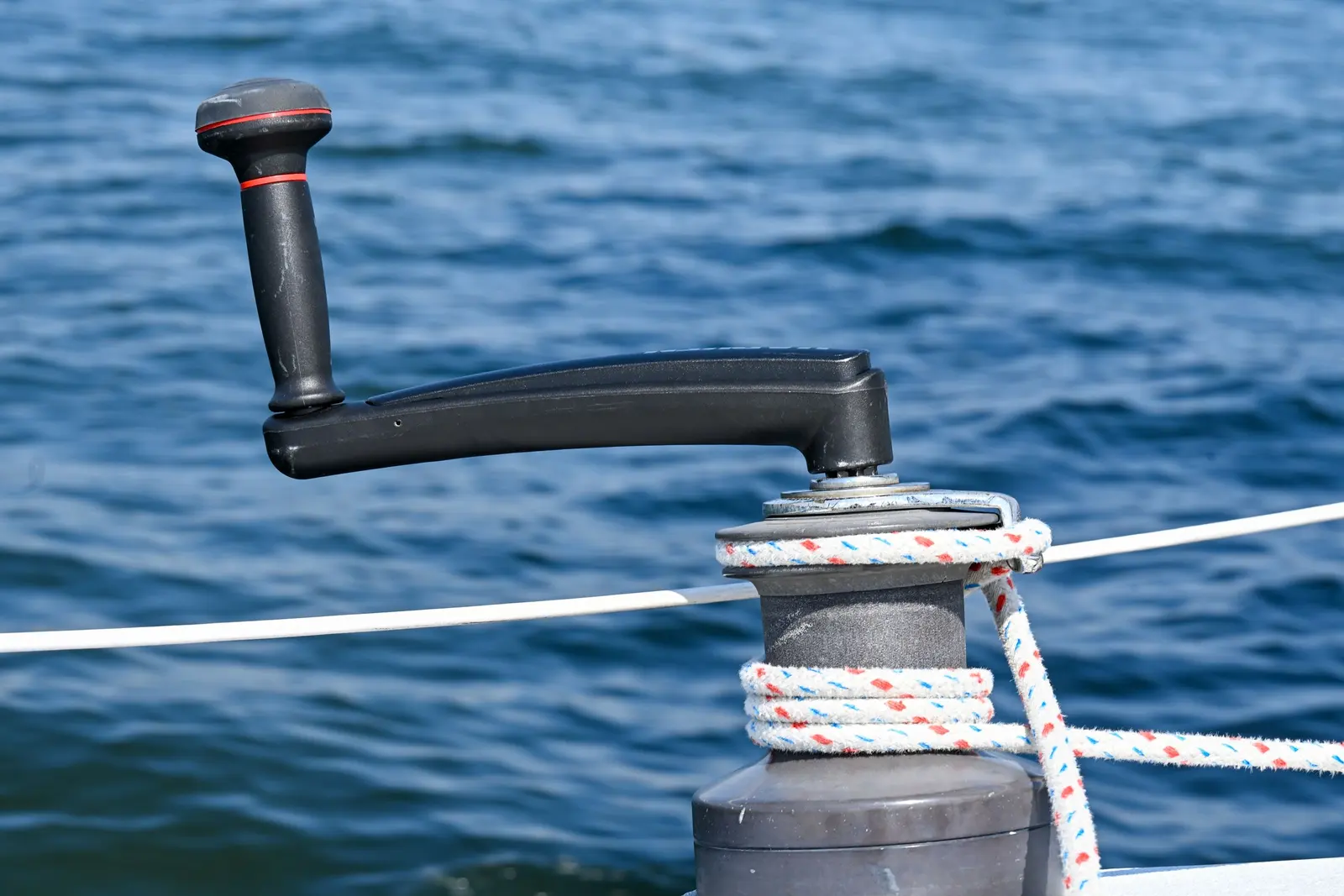 Winch con la manovella inserita e la scotta bianca e rossa avvolta, mare blu sullo sfondo