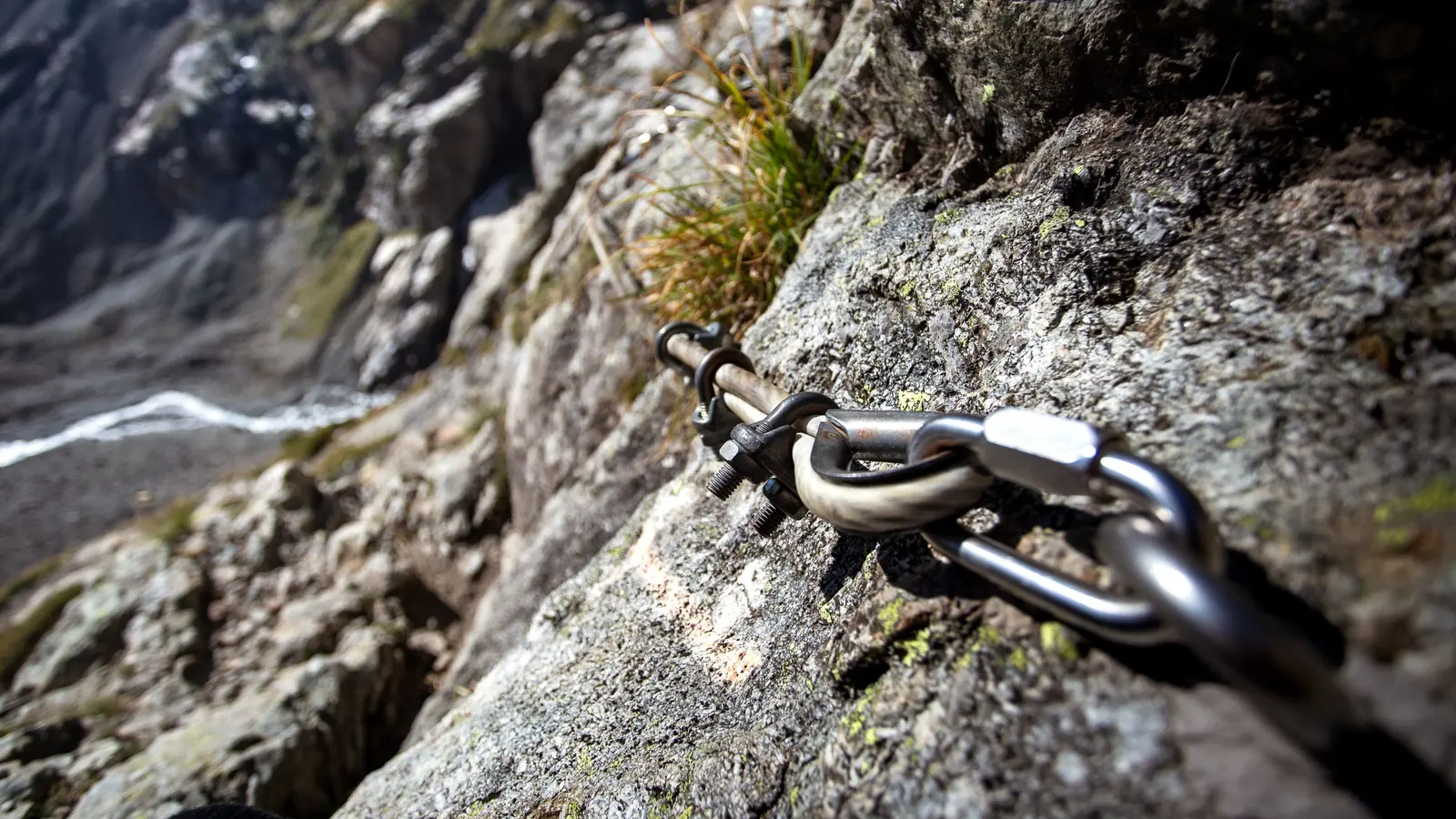 Il cavo d'acciaio di una ferrata fissato alla roccia con un ancoraggio, sullo sfondo la valle