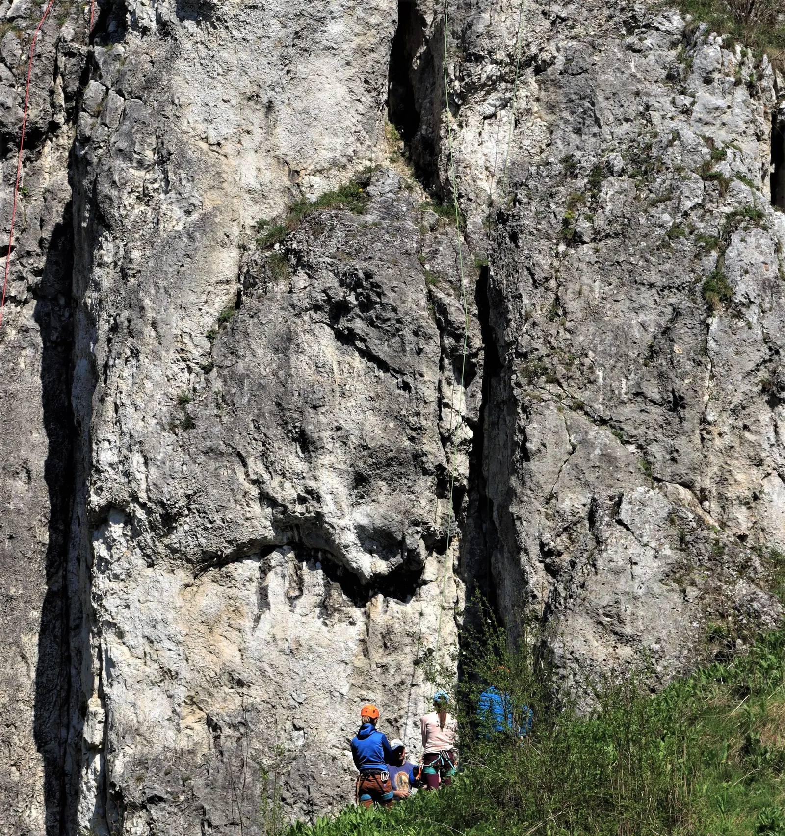 Parete calcarea alta e chiara, alla base un piccolo gruppo con caschi e corde