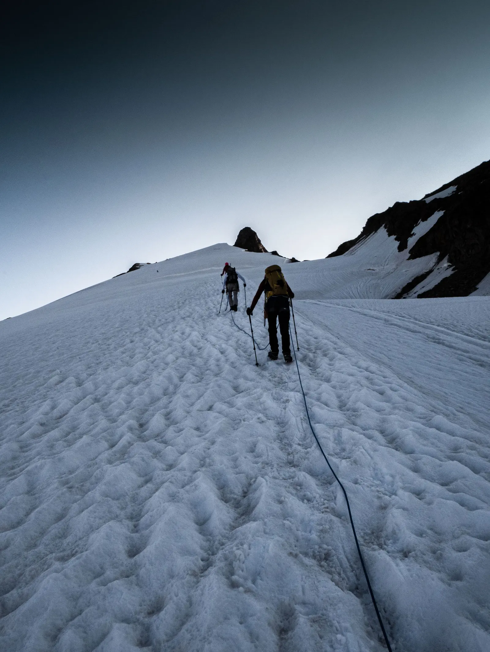Due alpinisti legati in cordata camminano su un ghiacciaio, la corda tesa tra loro