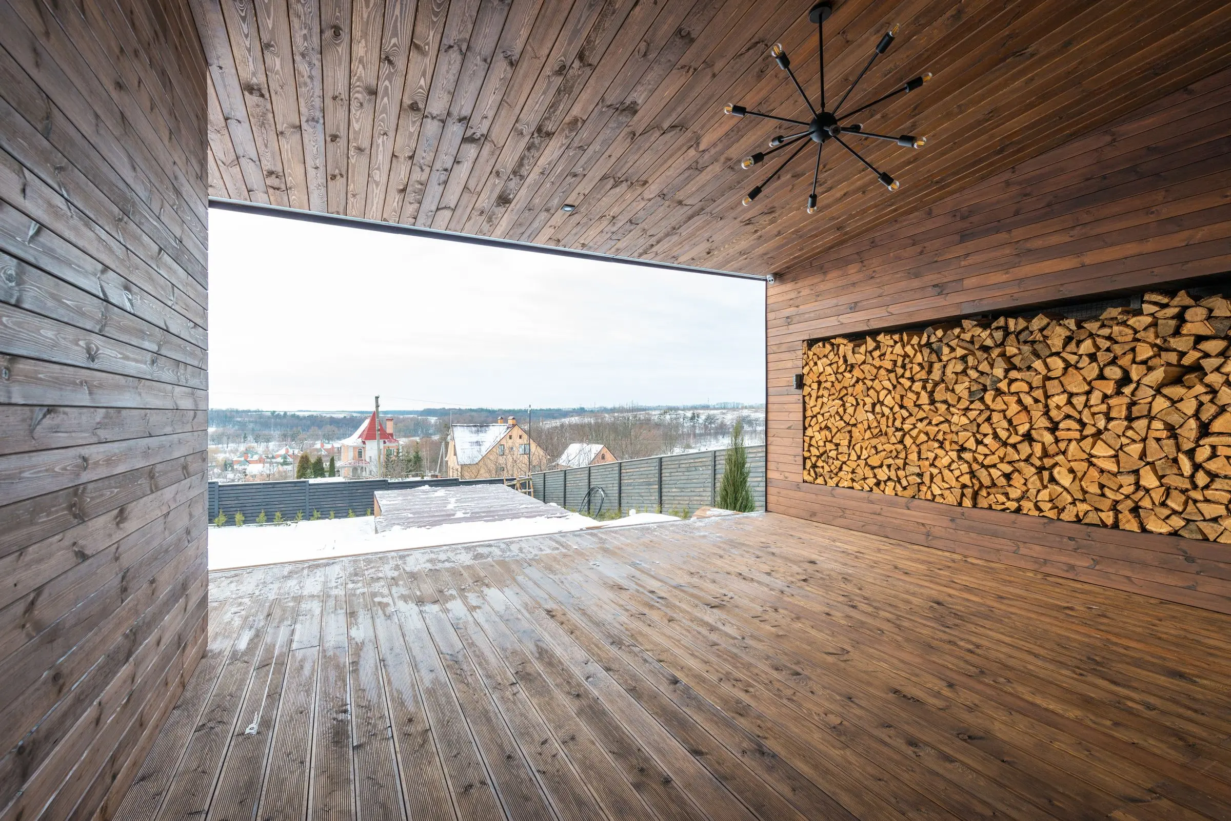 Loggia coperta in legno con legnaia a parete e vista sui tetti innevati